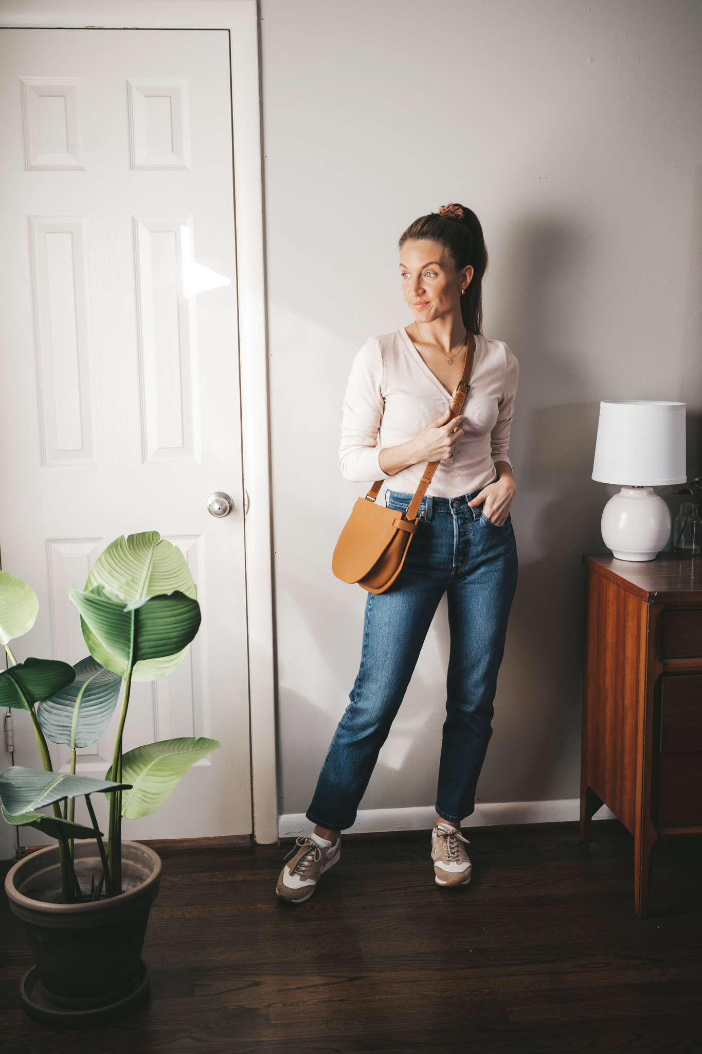 winter capsule wardrobe outfit with an ivory henley bodysuit, straight denim, and white and tan leather sneakers with a cognac crossbody bag