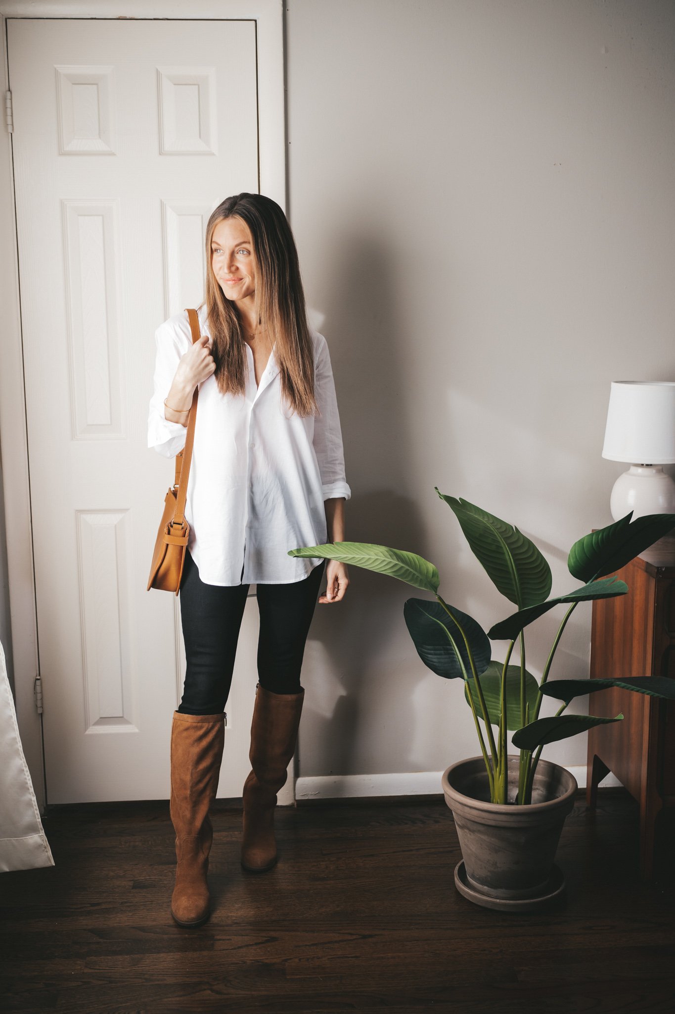 a mini capsule wardrobe outfit with a white button down, black skinny jeans, brown suede knee high boots and a cognac crossbody bag