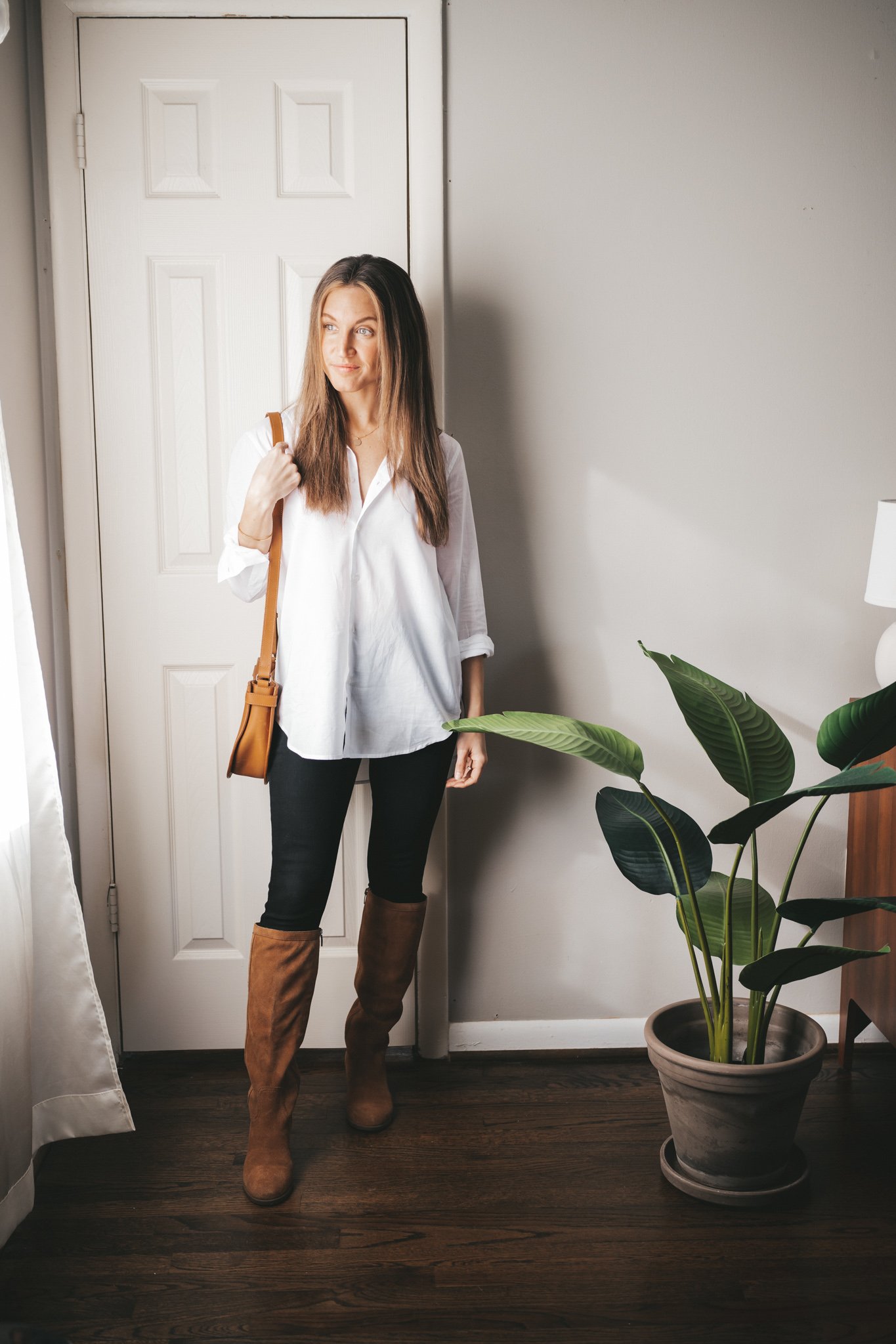 a mini capsule wardrobe outfit with a white button down, black skinny jeans, brown suede knee high boots and a cognac crossbody bag