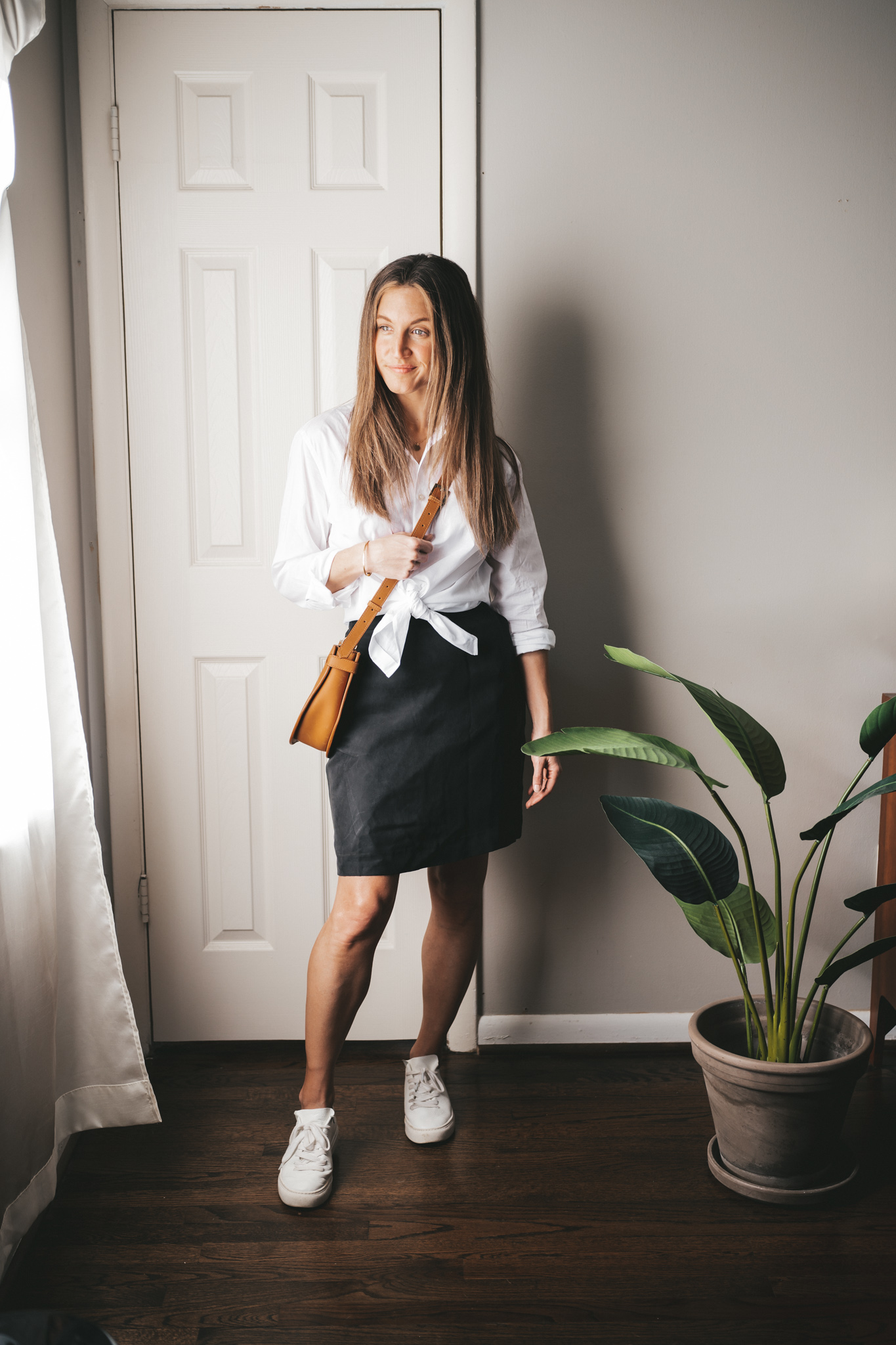 winter capsule wardrobe outfit with a white button down, black mini skirt, white sneakers, and cognac crossbody bag