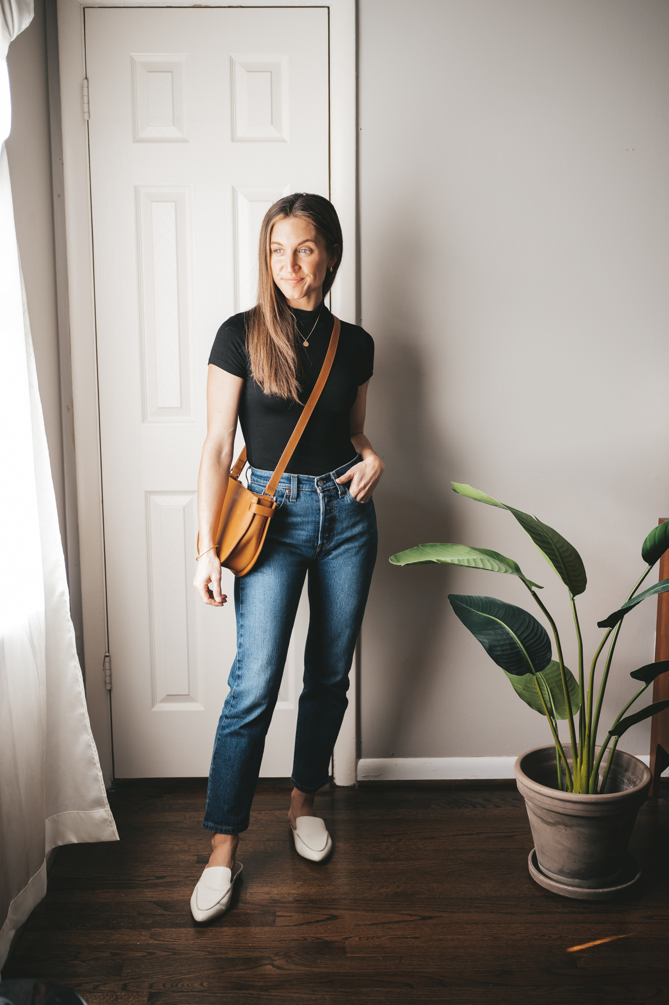 a winter mini capsule wardrobe outfit with a black polo tee, dark wash straight denim, and white mules with a cognac crossbody bag