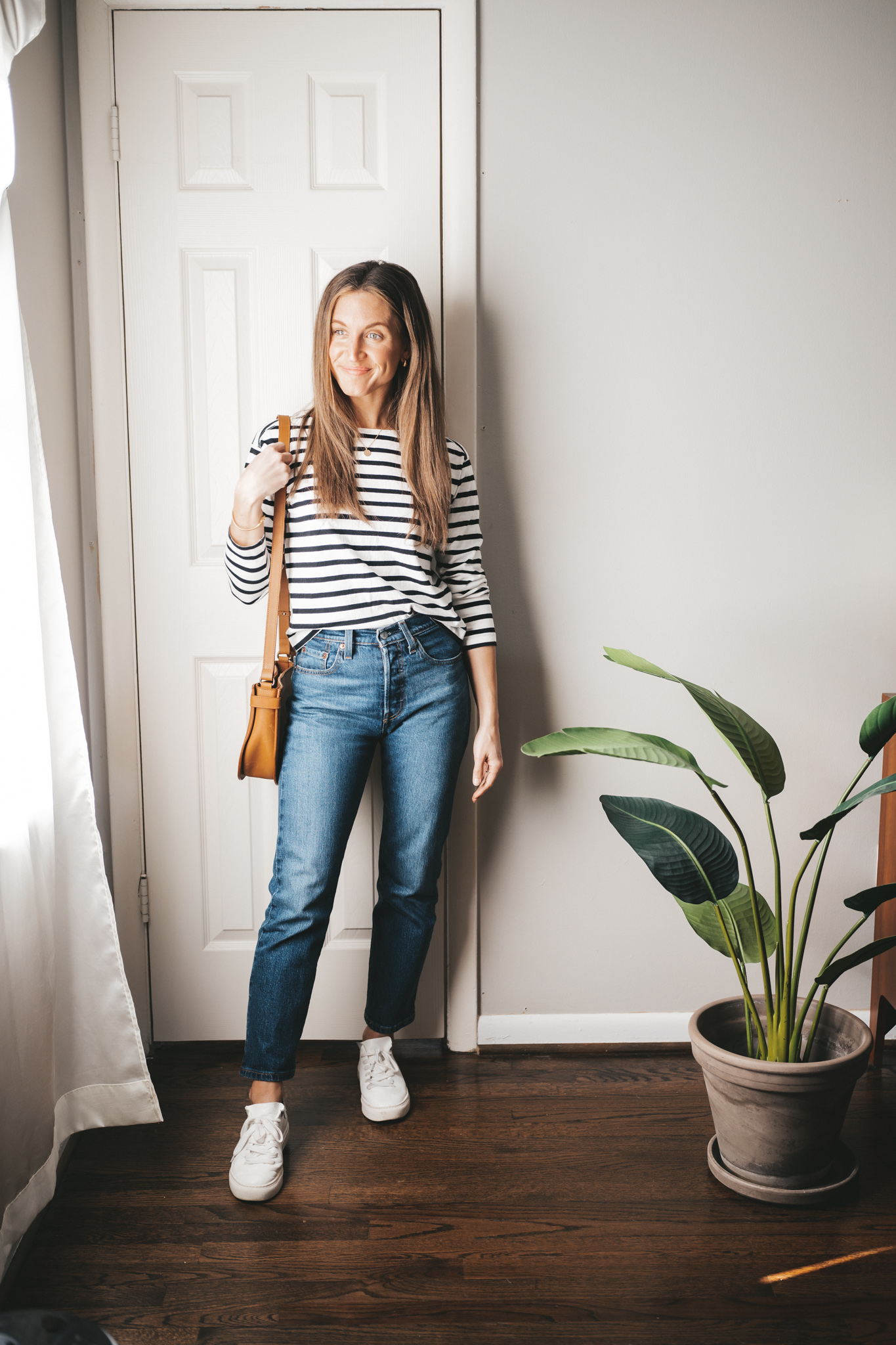 a mini capsule wardrobe outfit with a black and white striped top, dark wash straight denim, white sneakers and a cognac crossbody bag