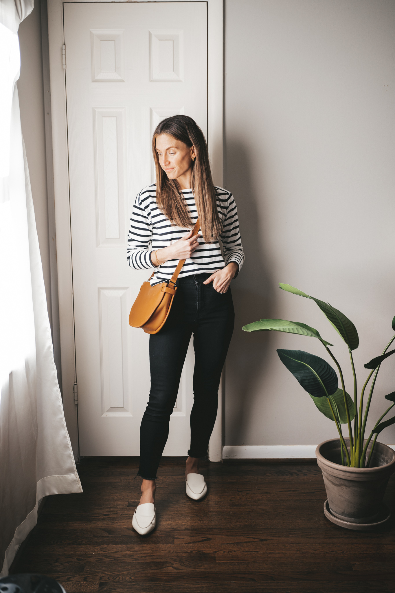 a winter mini capsule wardrobe outfit with a striped top, black skinny jeans, white mules, and a cognac crossbody bag