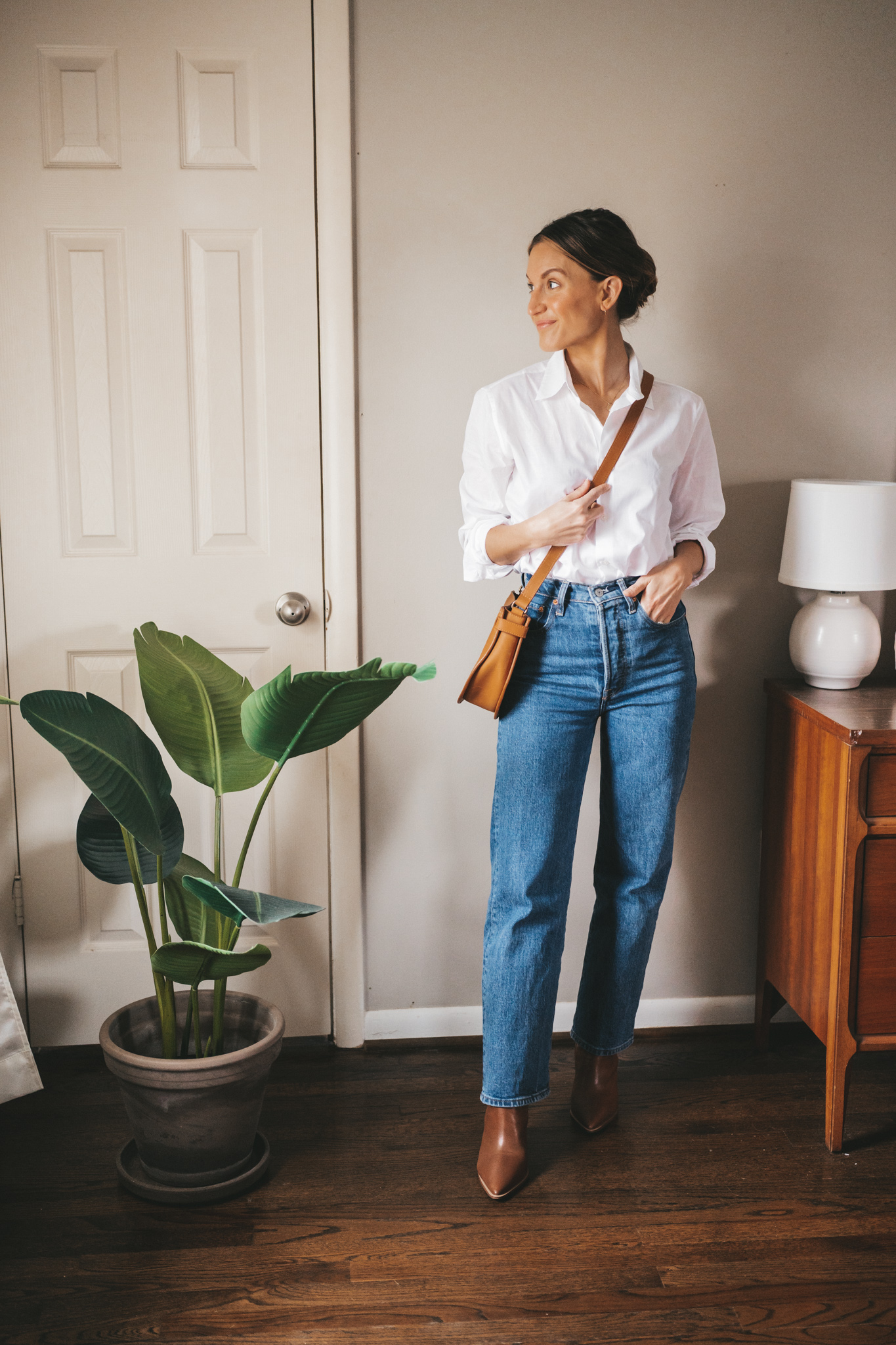 winter outfit with a white button down, high waisted straight leg denim, brown heeled ankle boots, and a cognac crossbody bag