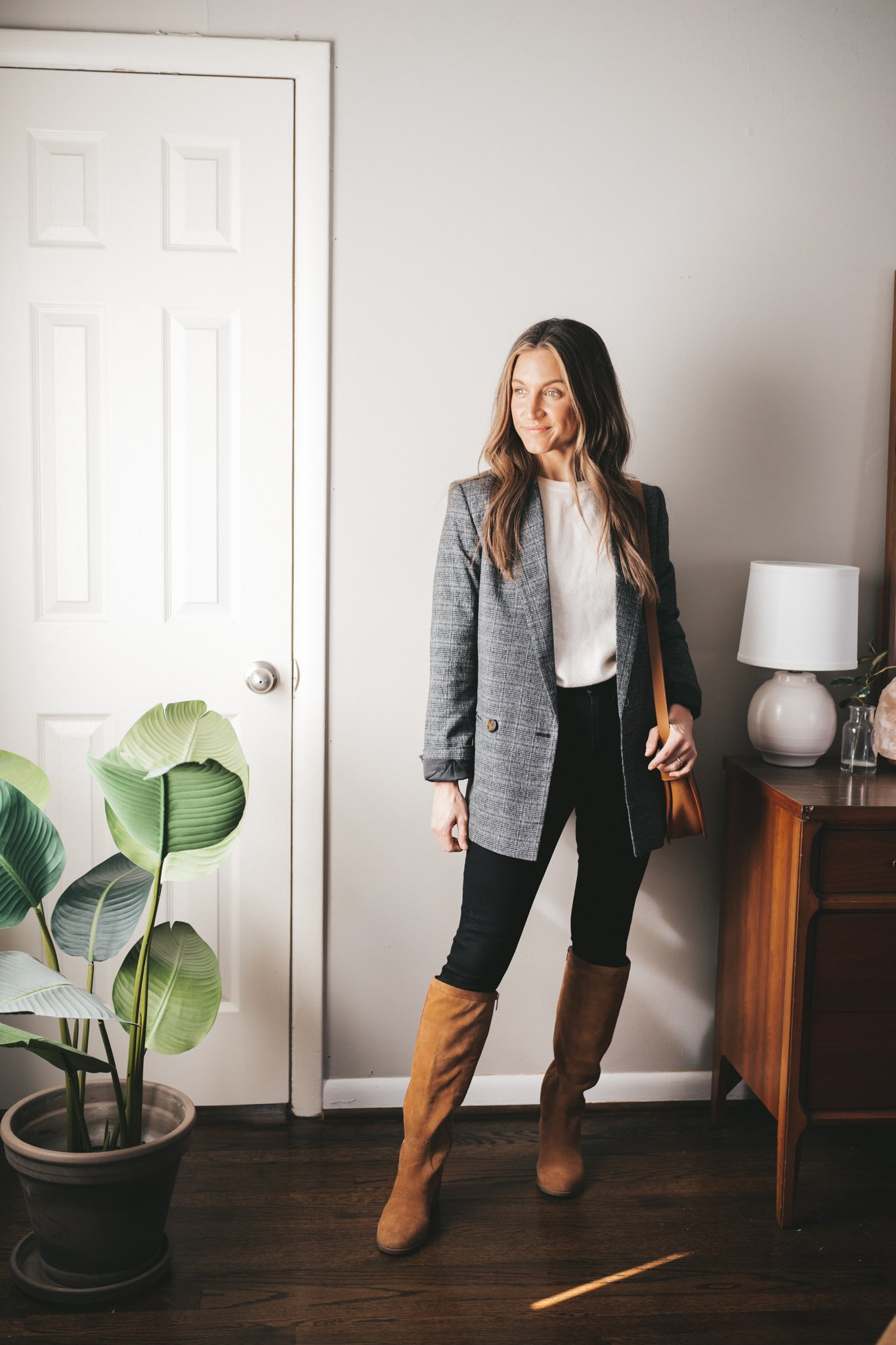 blazer outfit idea with a gray plaid blazer, cream cashmere crewneck sweater, black skinny jeans, brown suede knee high boots, and a cognac crossbody bag