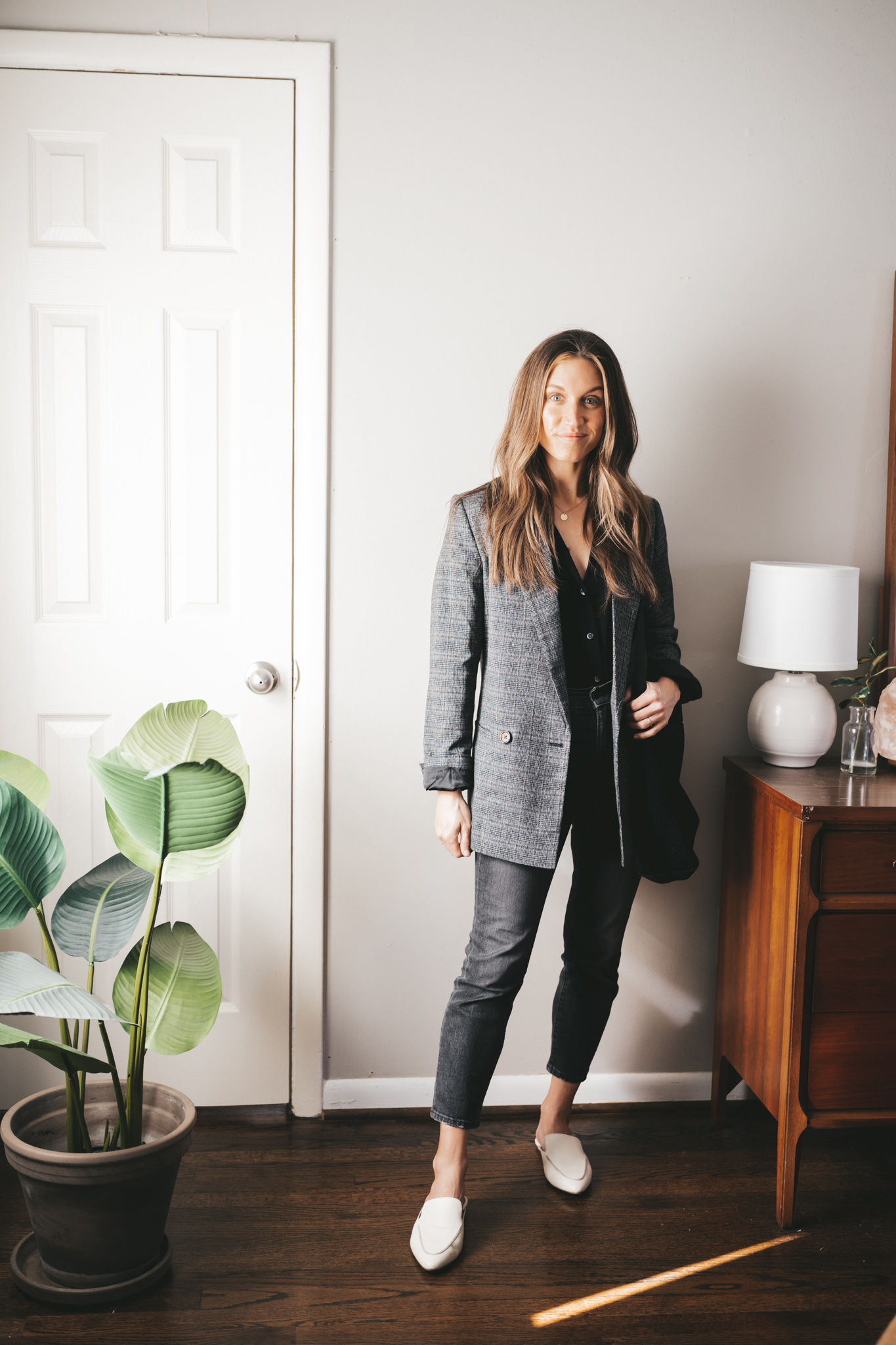 blazer outfit idea with a black button down, washed black denim, a plaid blazer, and white mules