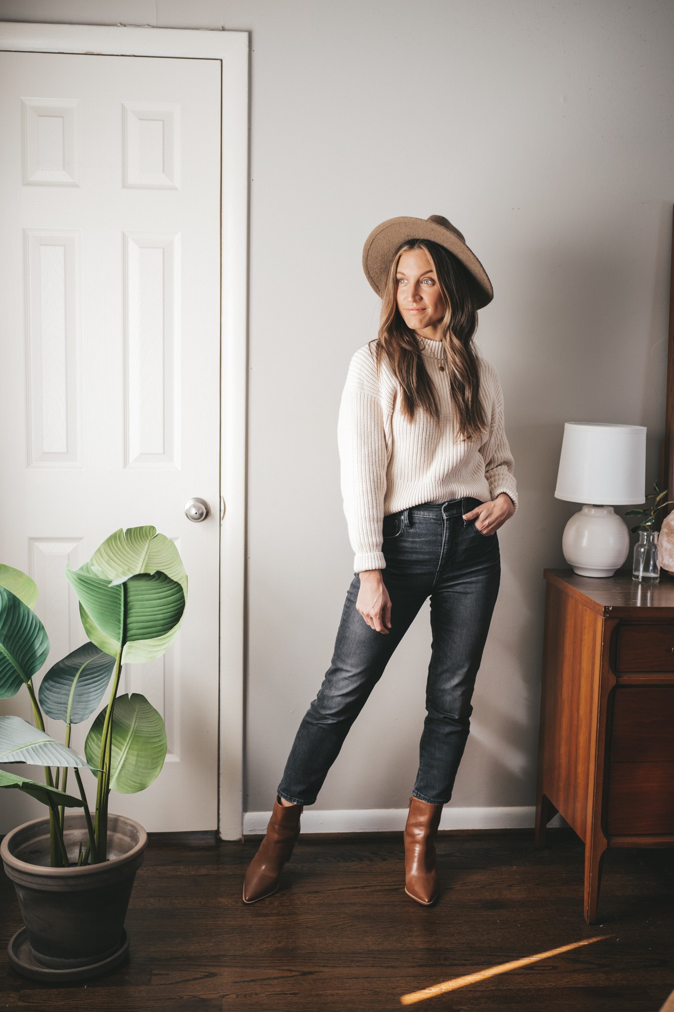 winter outfit with a cream colored sweater, washed black denim, brown heeled ankle boots, and a taupe fedora