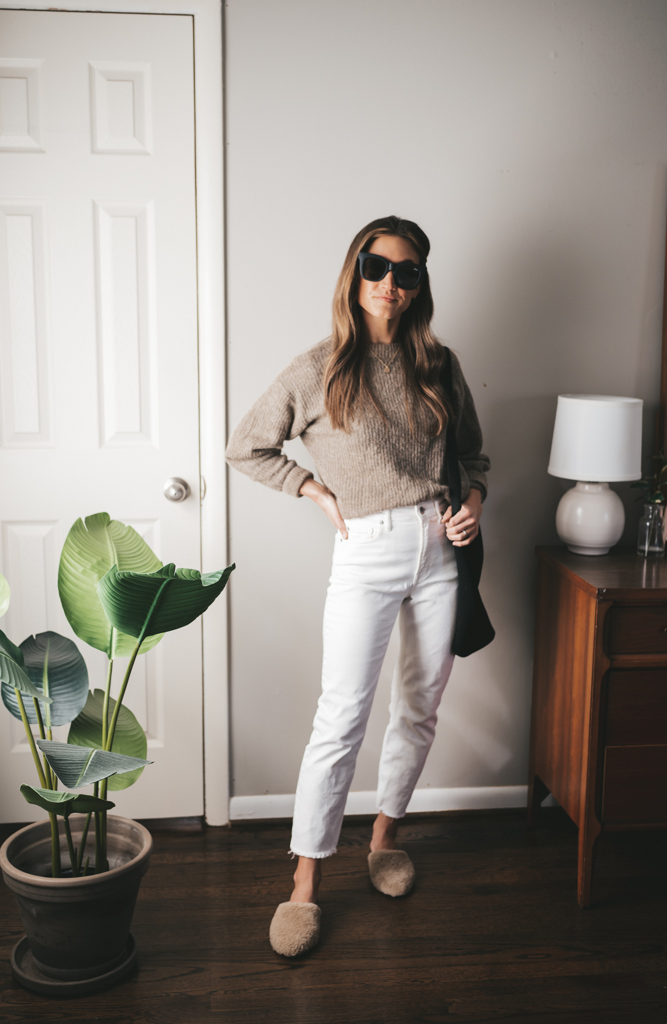 late winter outfit idea with a taupe alpaca sweater, white straight denim, shearling mules, a black tote bag, and black square frame sunglasses