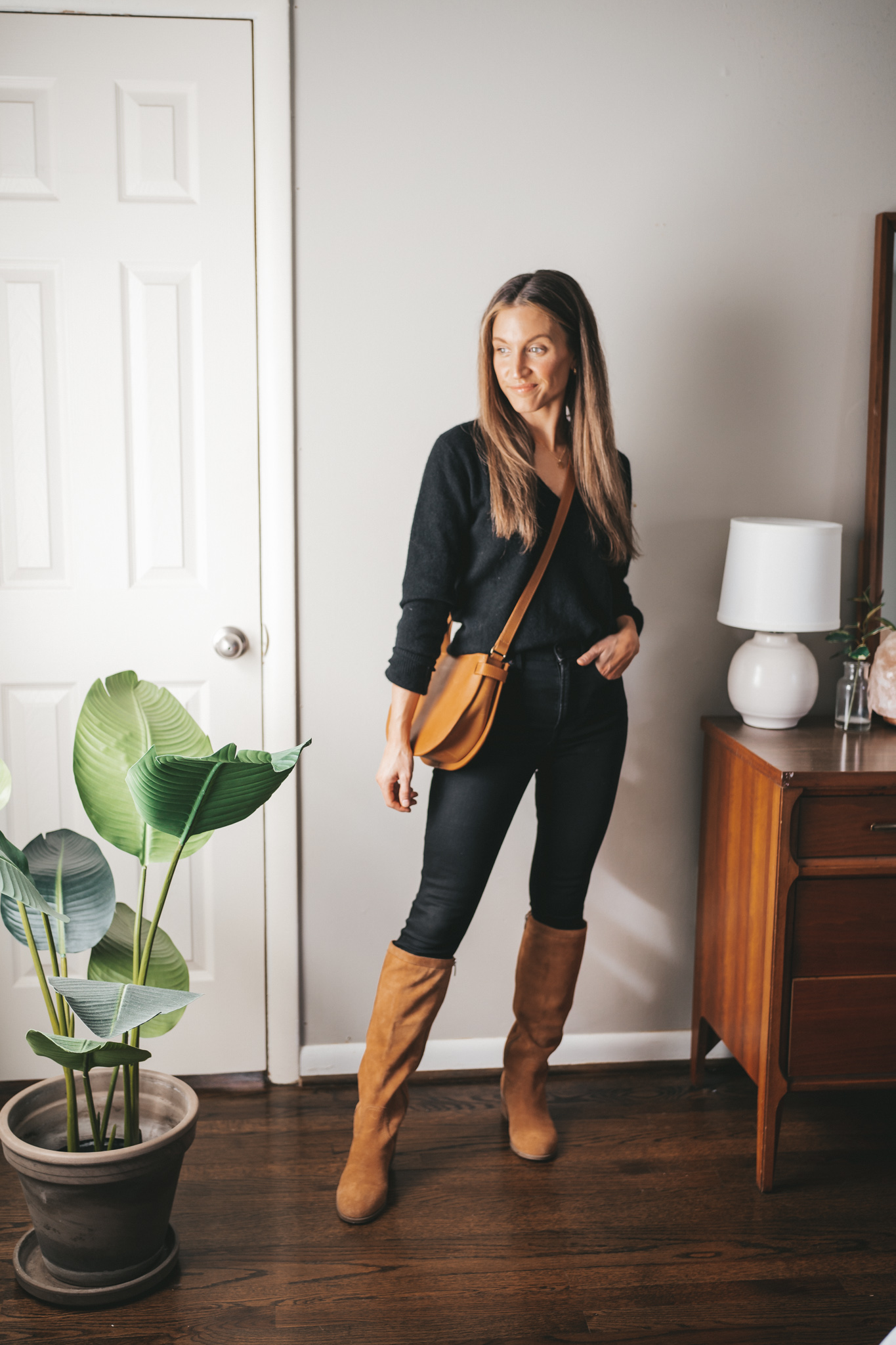 late winter outfit idea with a black v-neck sweater, black skinny jeans, brown suede knee high boots, and a cognac crossbody bag