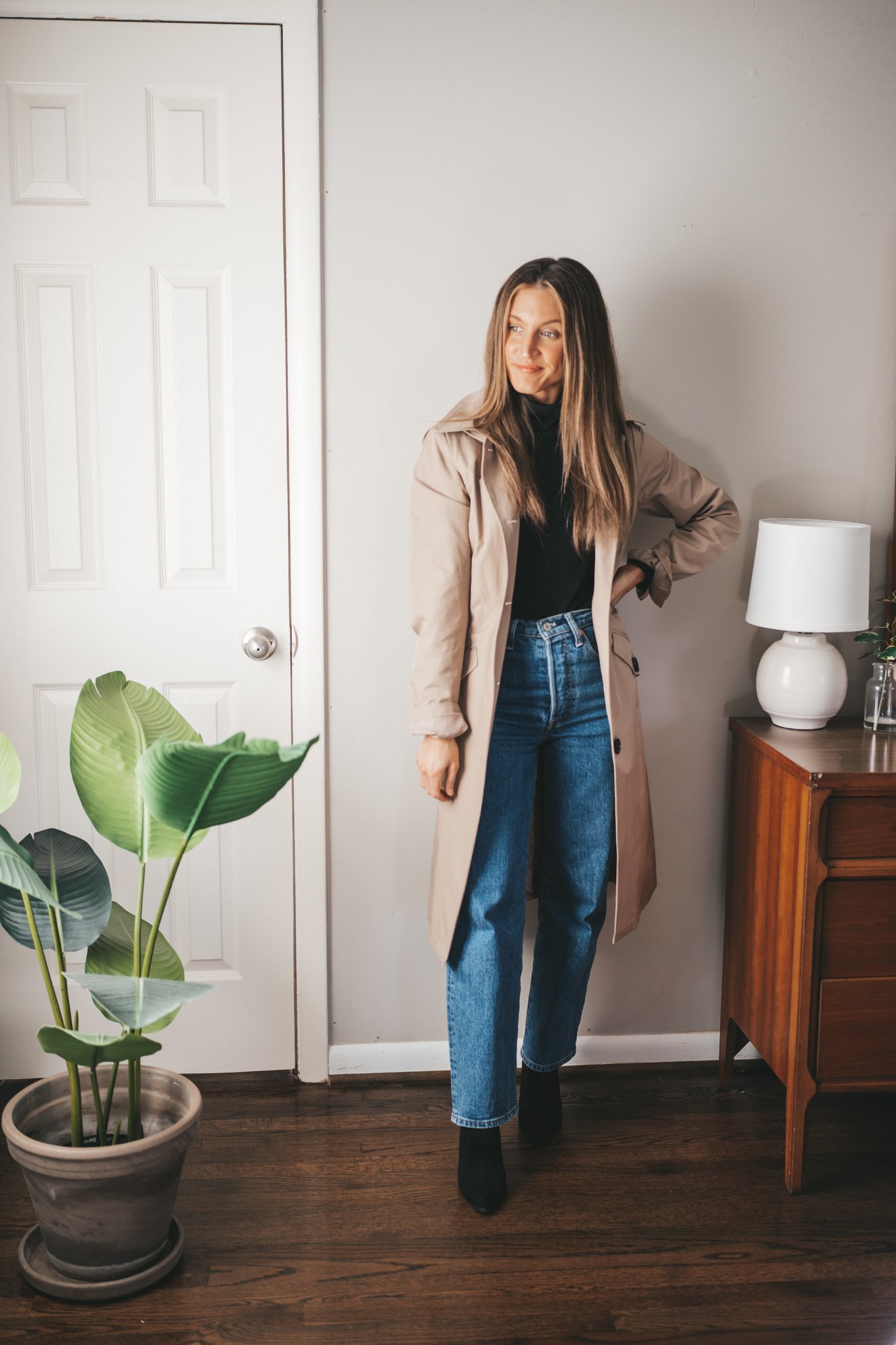 ashley wearing an outfit with a black turtleneck, tan trench coat, straight denim, and black ankle boots