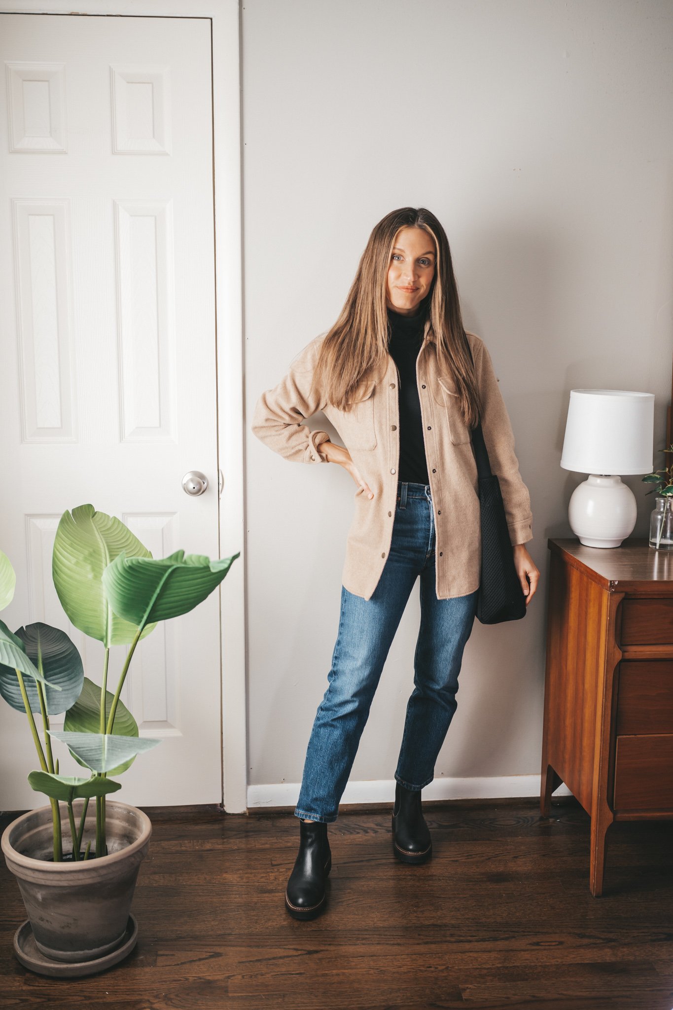 ashley wearing a black turtleneck outfit with a tan shacket, mom jeans, and lug sole boots with a black mesh tote bag