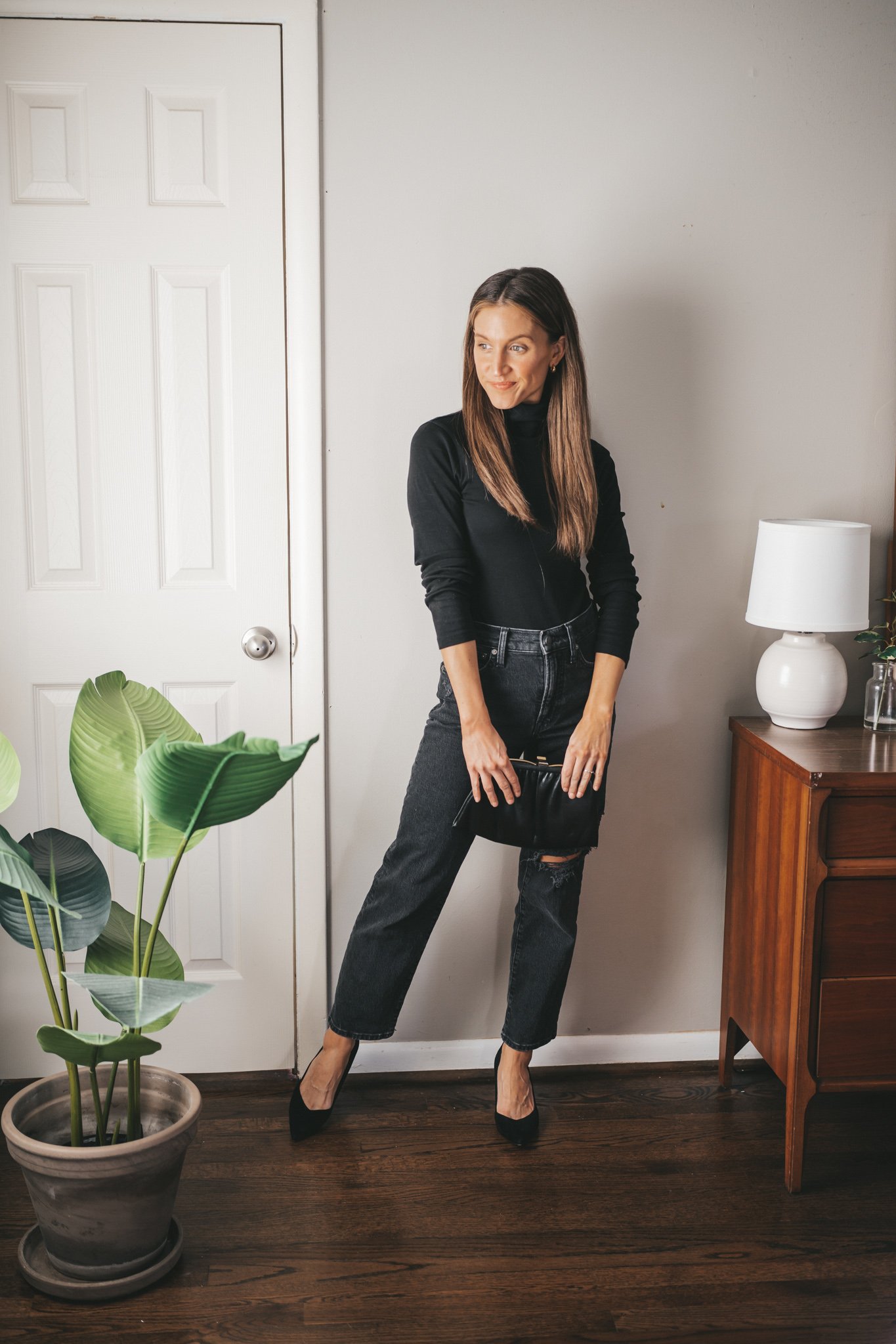 ashley wearing a black turtleneck outfit with distressed black straight denim, black pumps, and a black vintage clutch