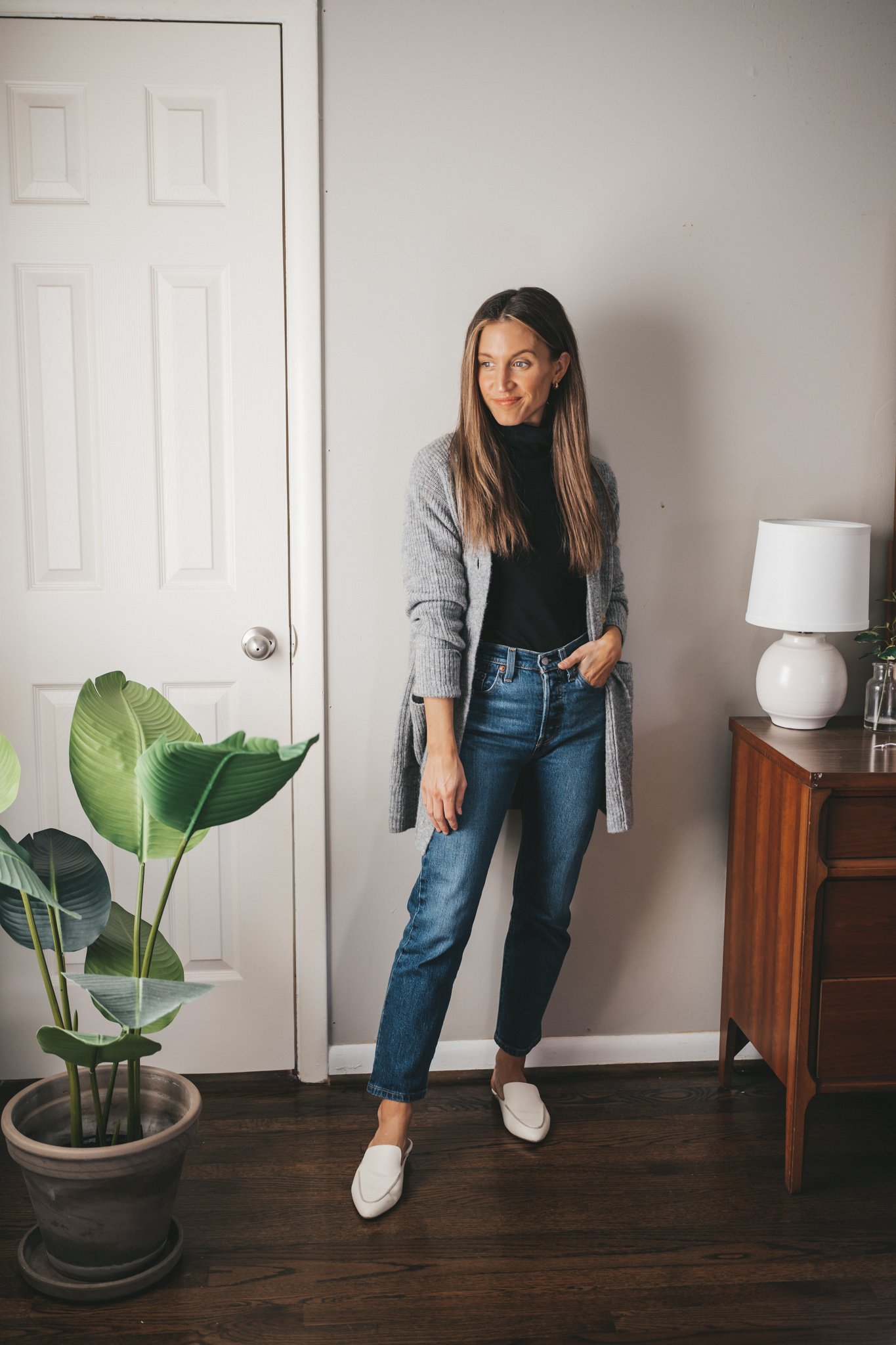 ashley wearing a black turtleneck outfit with a gray cardigan, dark wash denim, and white mules