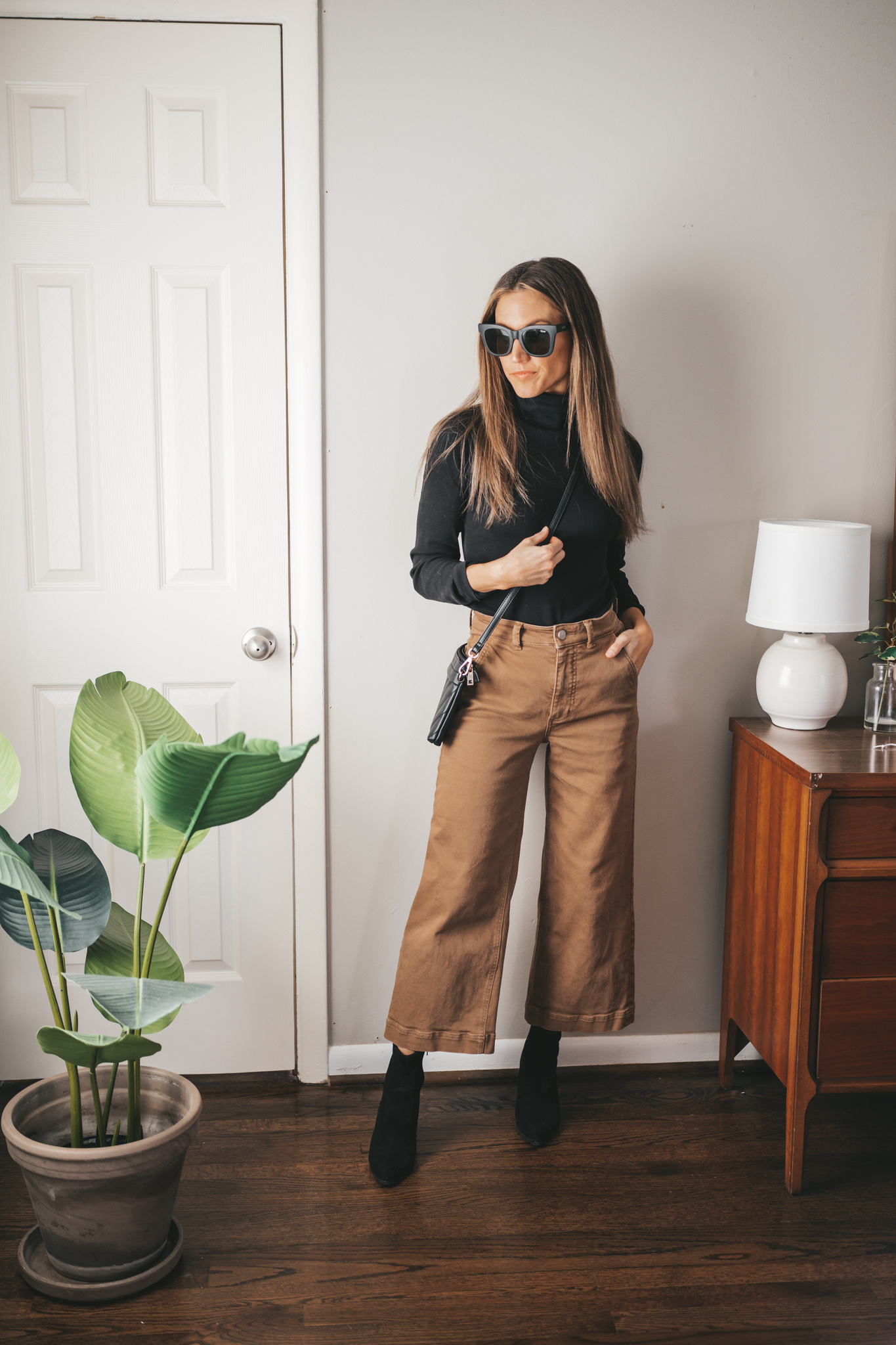 ashley wearing a black turtleneck outfit with brown wide leg cropped pants, black heeled ankle boots, and a black quilted crossbody bag