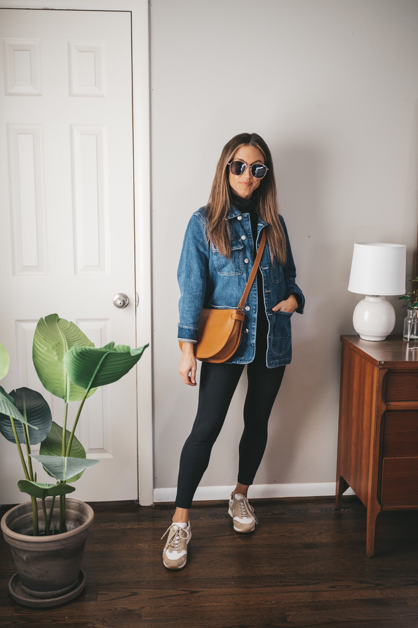 ashley wearing a black turtleneck outfit with a denim jacket, leggings, white and tan leather sneakers, and a cognac crossbody bag