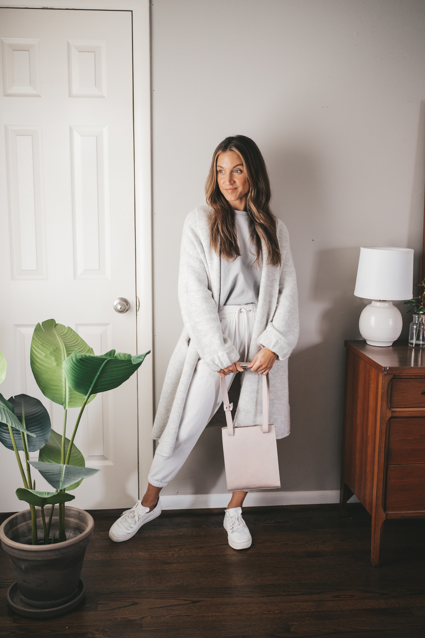 ashley wearing a light gray sweatshirt, light gray sweater coat, white joggers, and white sneakers carrying a gray shoulder bag