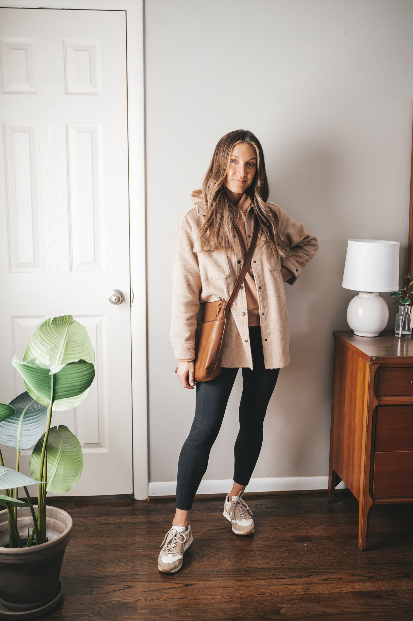 late winter outfit idea with a tan hoodie, tan shacket, black leggings, white and tan leather sneakers, and a brown crossbody bag