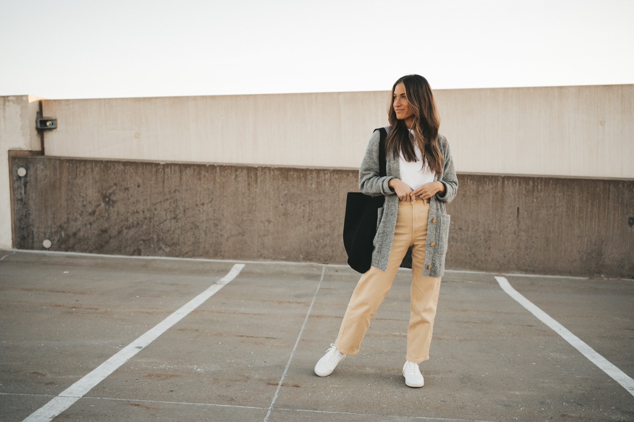ashley wearing the Everlane Way High Jean, a white tee, gray cardigan, and white sneakers standing on the roof of a parking garage