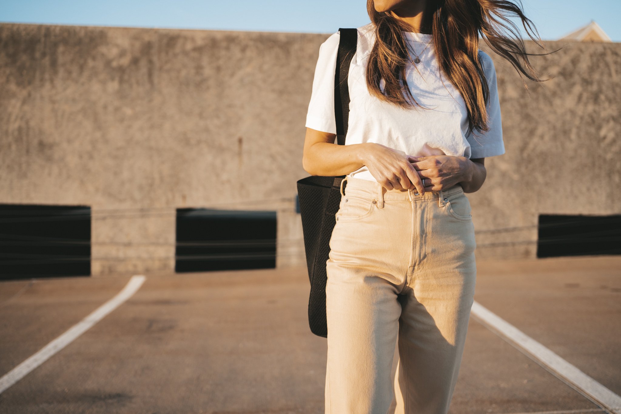 ashley wearing the Everlane Way High Jean, a white tee, and white sneakers standing on the roof of a parking garage