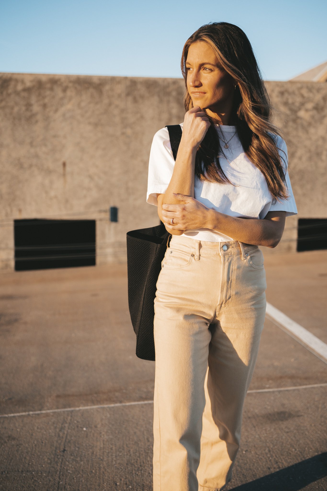 ashley wearing the Everlane Way High Jean, a white tee, and white sneakers standing on the roof of a parking garage