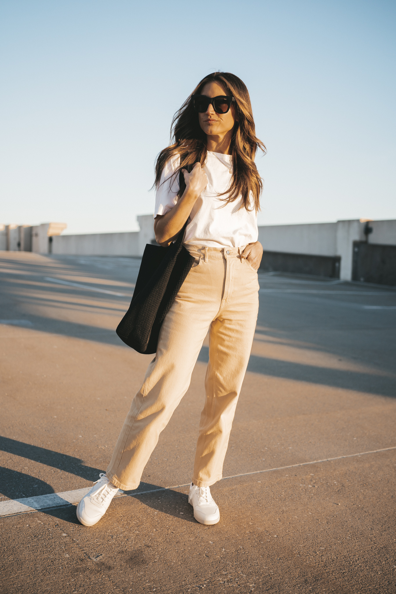 ashley wearing the Everlane Way High Jean, a white tee, and white sneakers standing on the roof of a parking garage