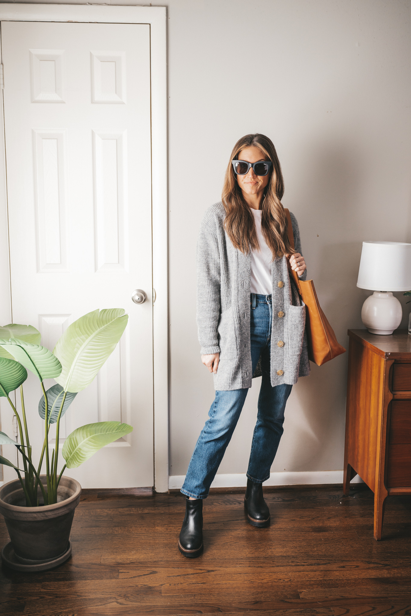spring outfit with a gray cardigan, white tee, dark wash denim, black lug-sole boots, and a cognac leather tote bag