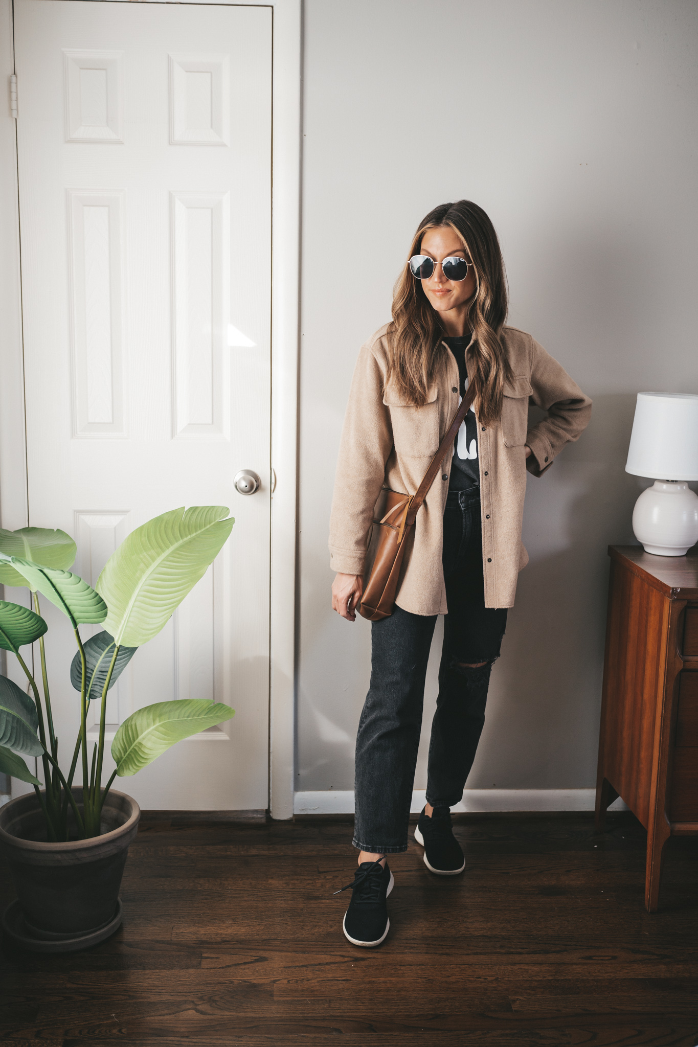 spring outfit idea with a black graphic tee, tan shacket, black distressed denim, black wool sneakers, and a brown leather crossbody bag