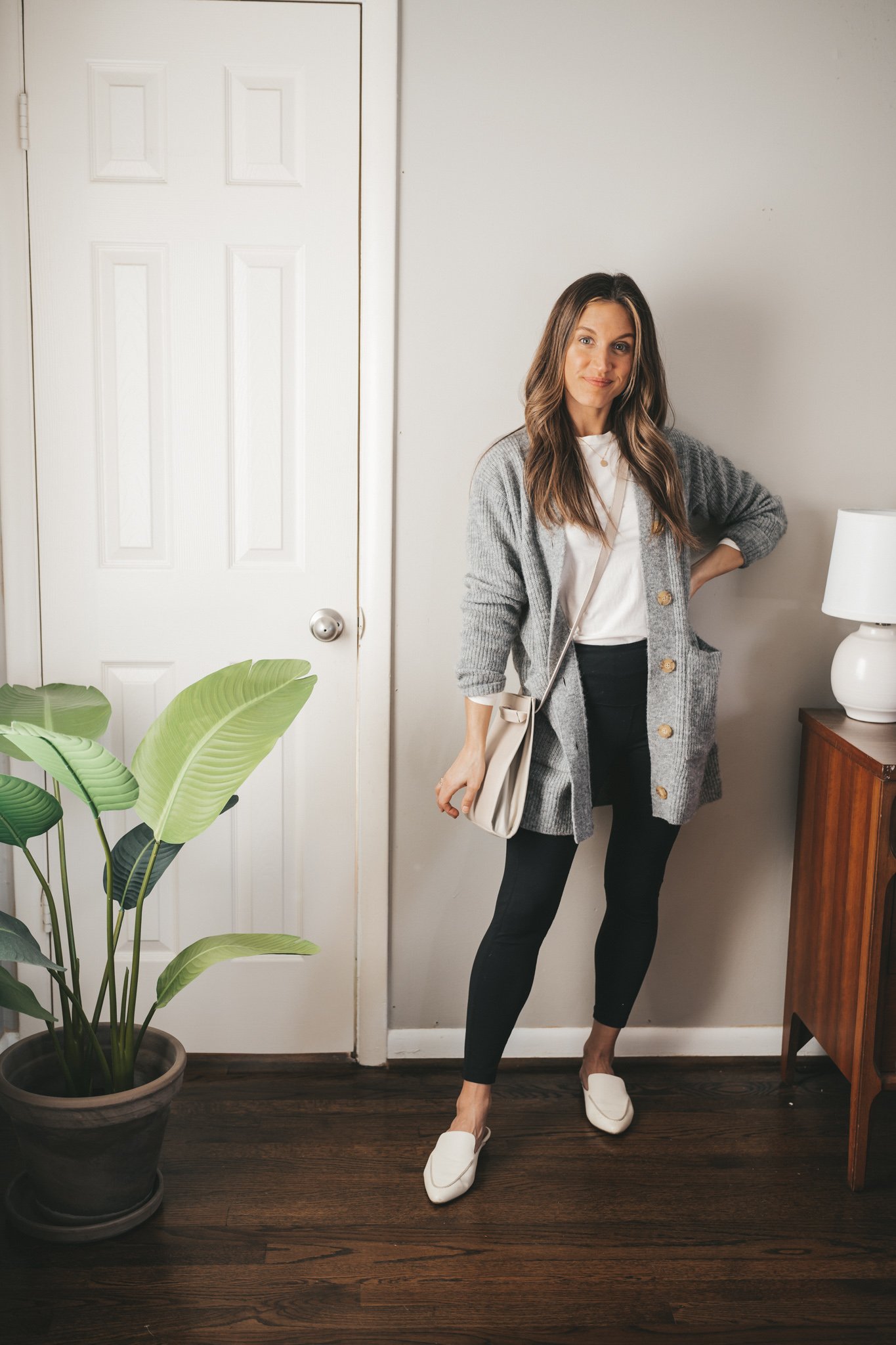 a work from home outfit with a white tee, gray cardigan, black leggings, and white mules with a light gray leather crossbody bag