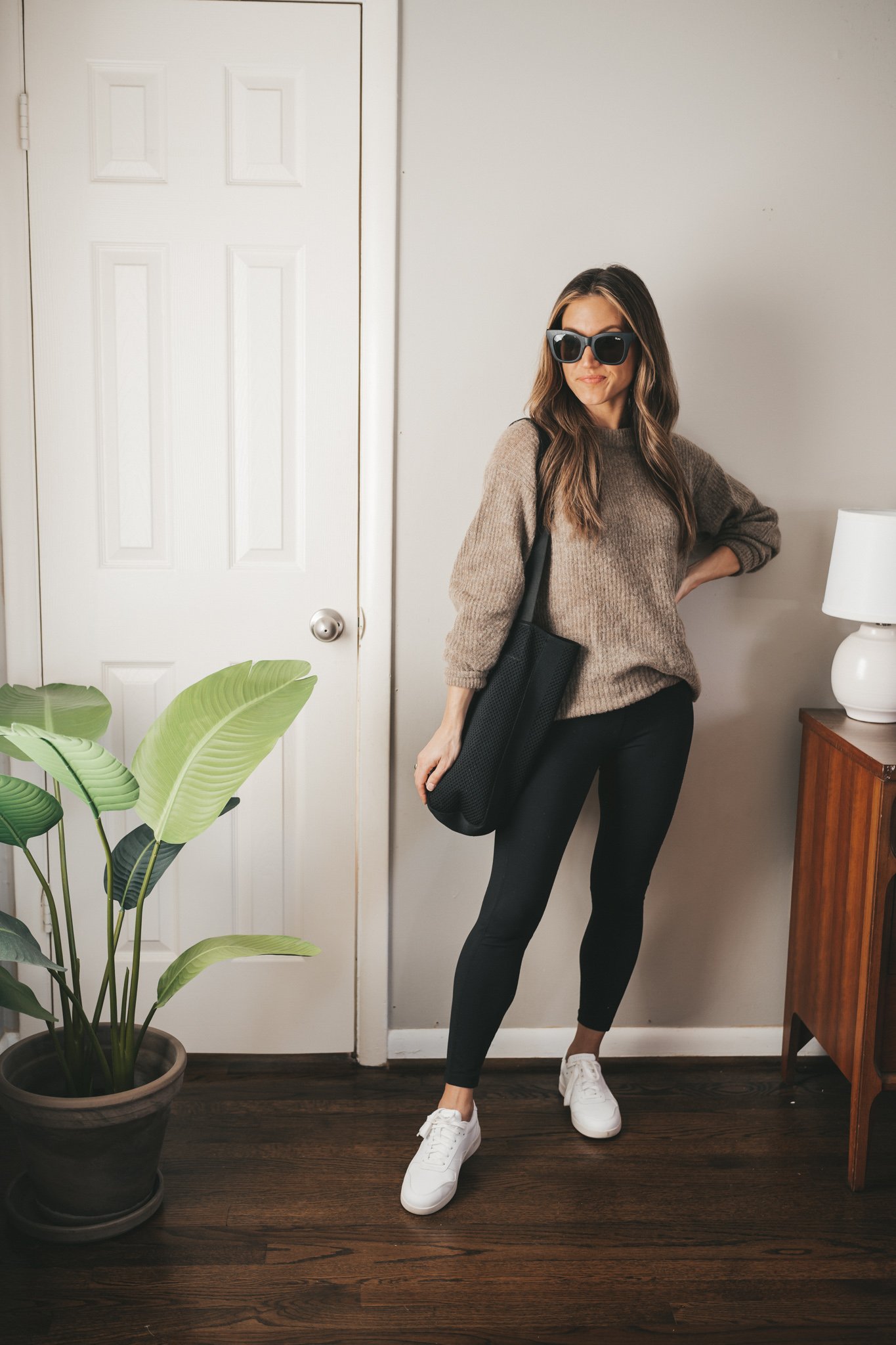 work from home outfit with a oversized taupe sweater, black leggings, white sneakers, black square frame sunglasses, and a black tote bag