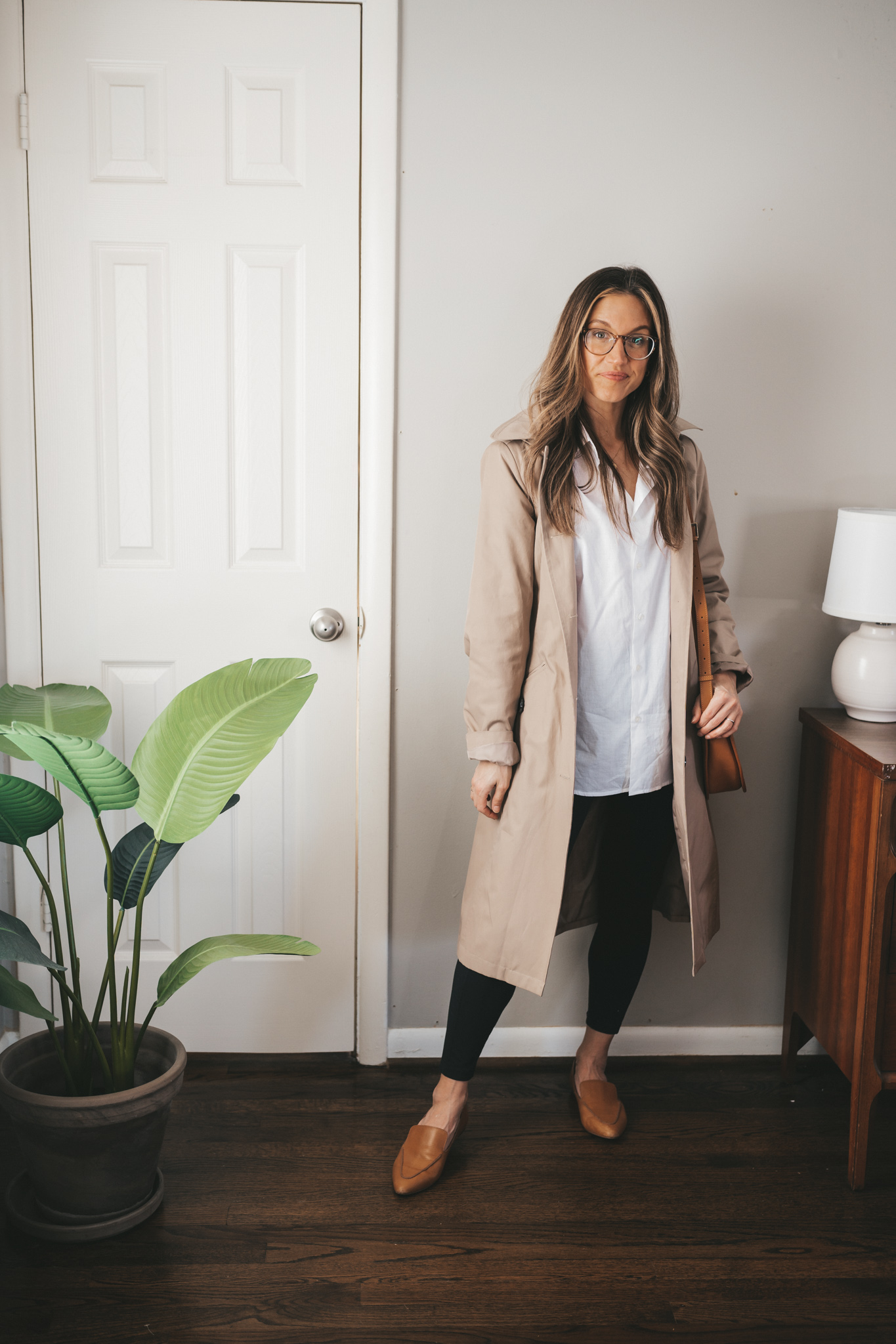 work from home outfit with a white button down, trench coat, black leggings, cognac loafers, and a cognac crossbody bag