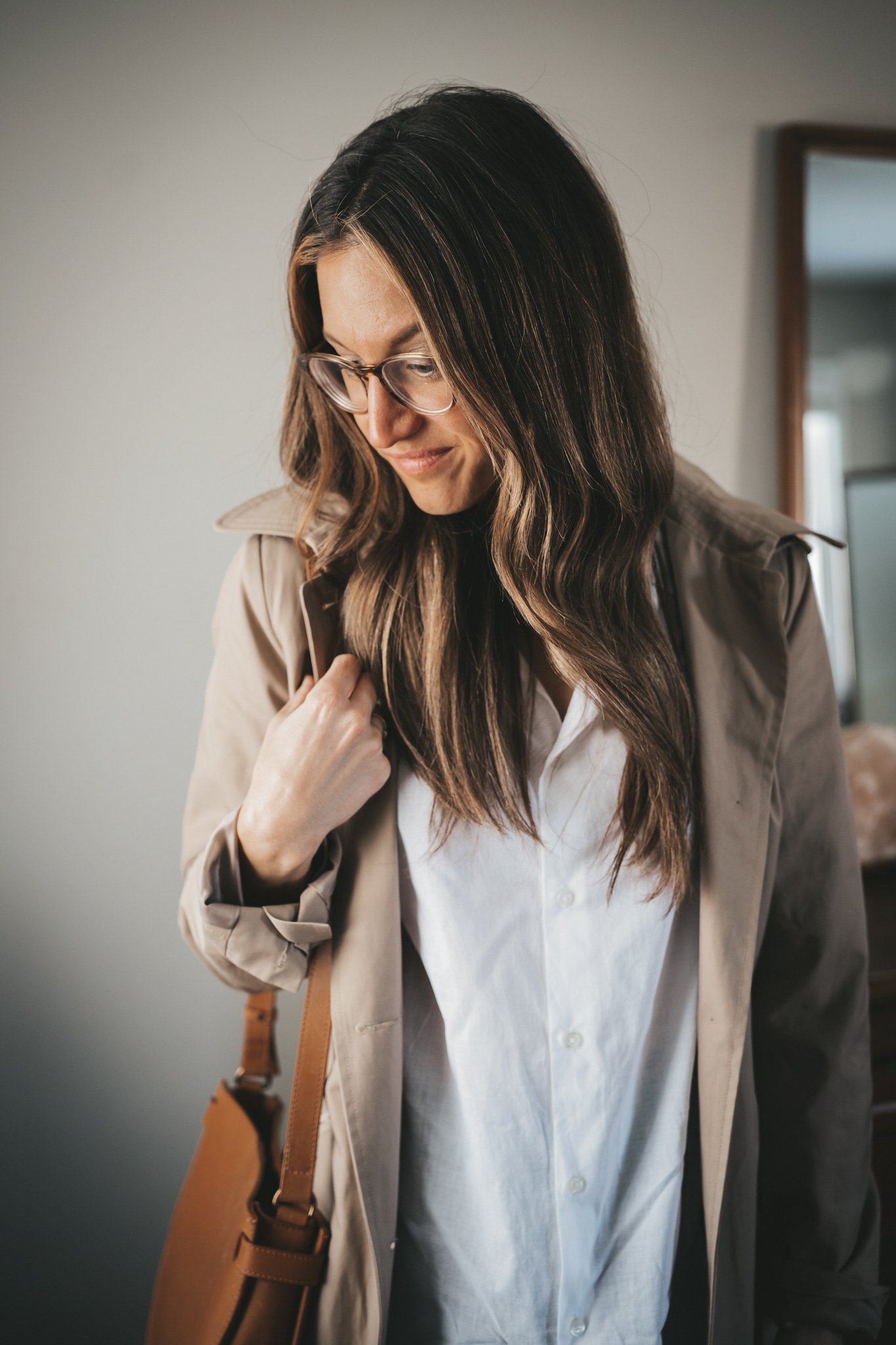 ashley wearing a white button down, trench coat, glasses, and a cognac crossbody bag
