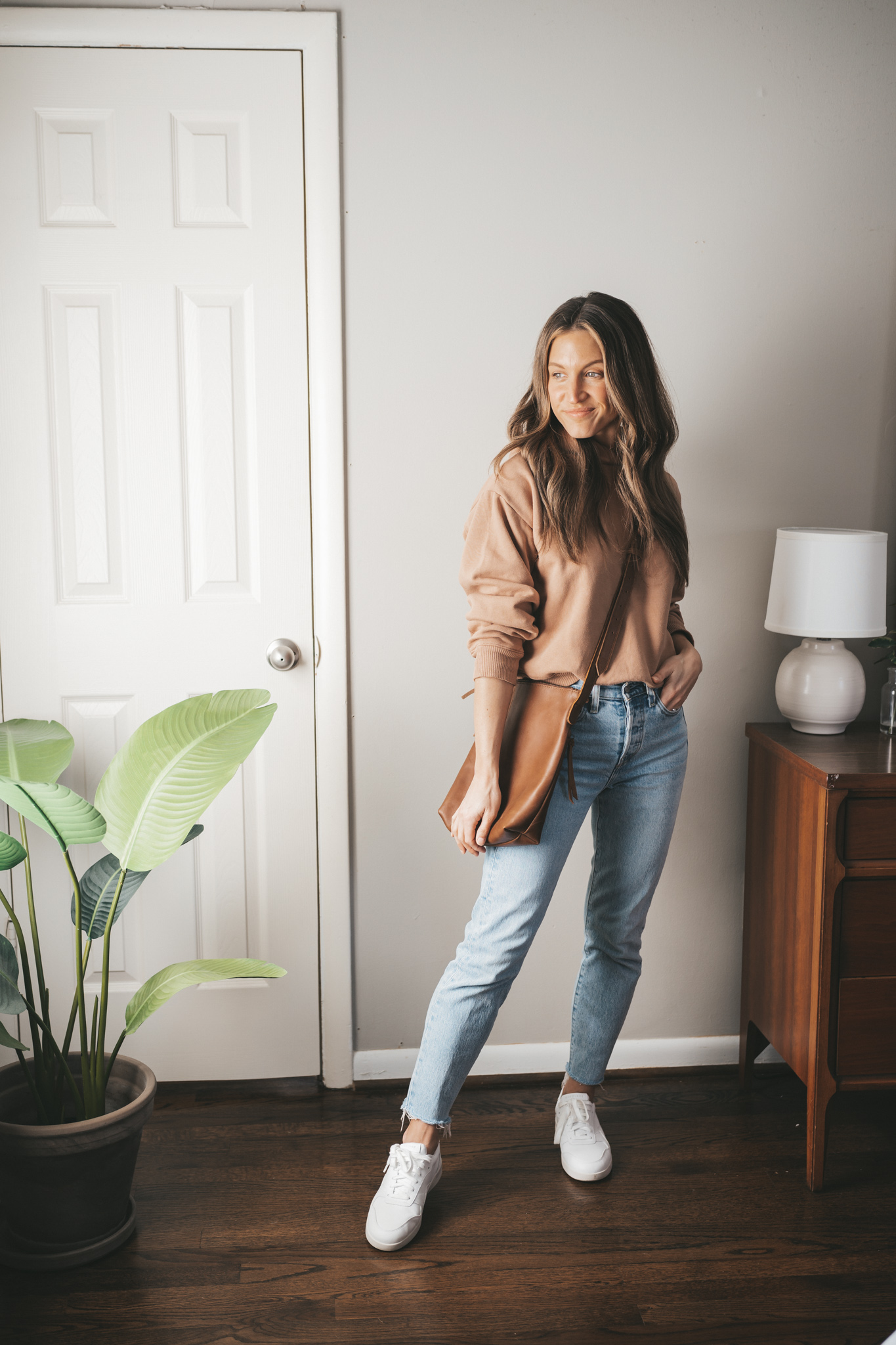 spring outfit idea with a tan hoodie, light wash mom jeans, white sneakers, and brown leather crossbody bag