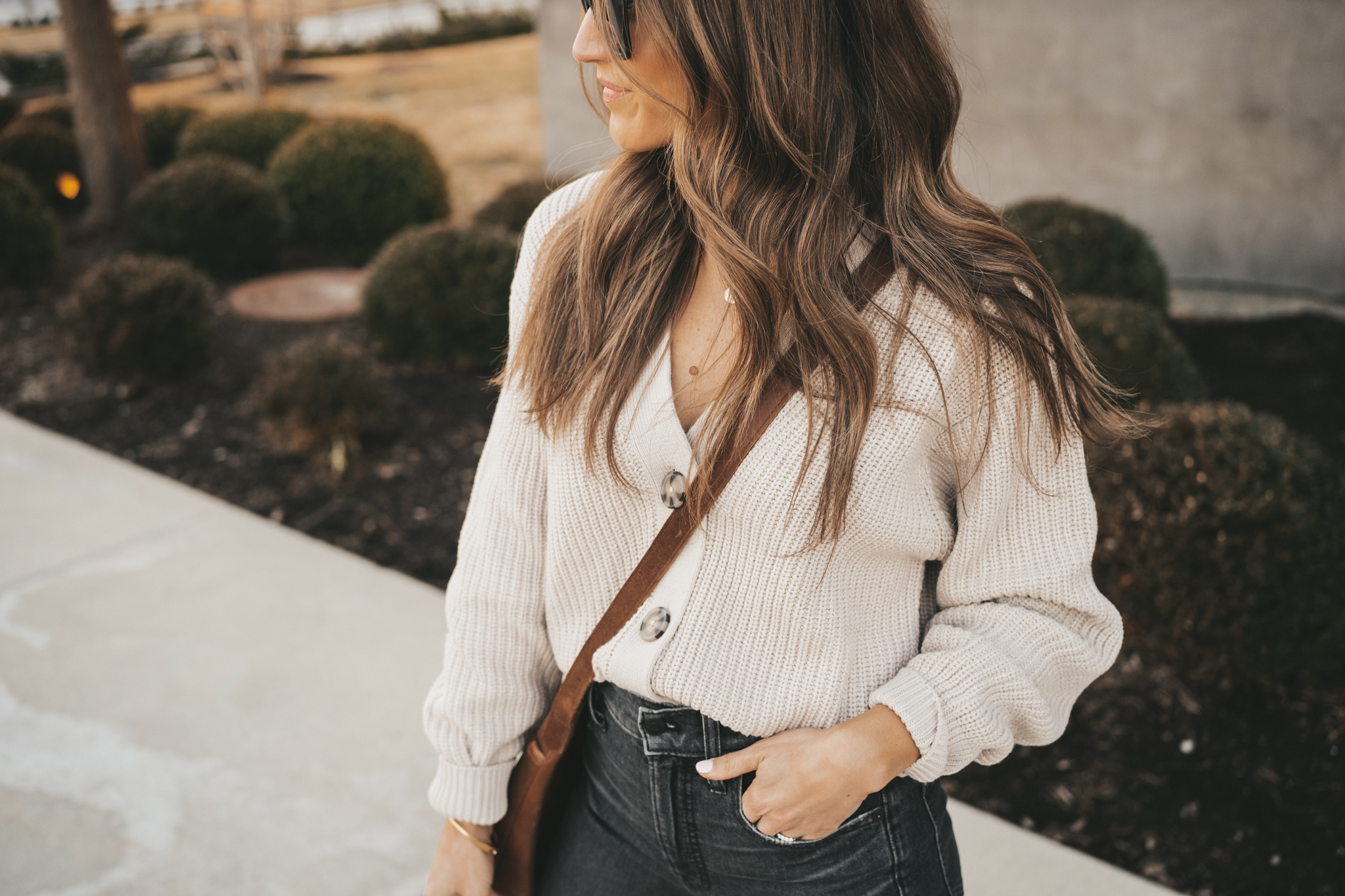 ashley wearing a taupe button front cardigan, black denim, white mules, and a brown crossbody body with black square frame sunglasses