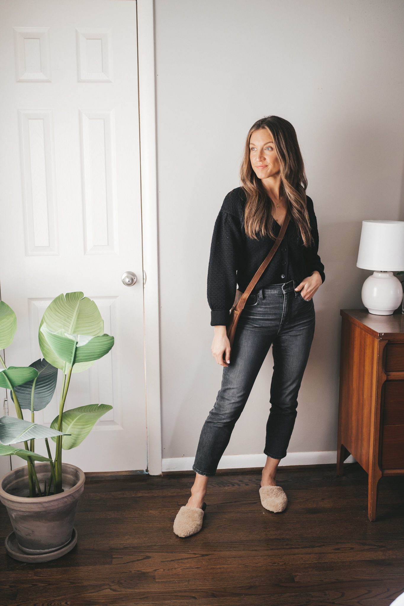 casual spring outfit idea with a black button front cardigan, washed black denim, tan shearling mules, and a brown crossbody bag
