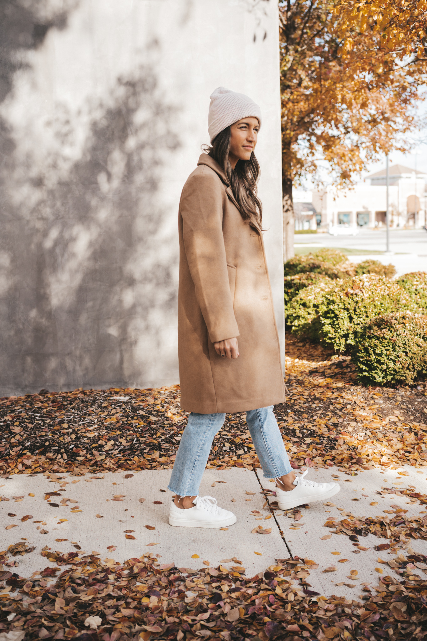 winter outfit with a camel coat, light wash denim, white sneakers, and a cream colored beanie