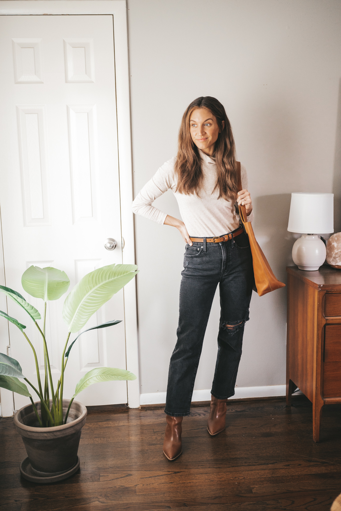 ashley wearing a turtleneck, black jeans, brown boots, and a brown tote bag