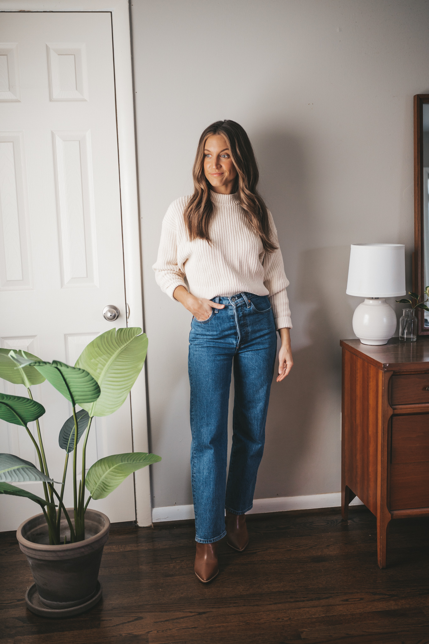 ashley wearing a cream colored sweater, dark wash straight denim, and brown ankle boots