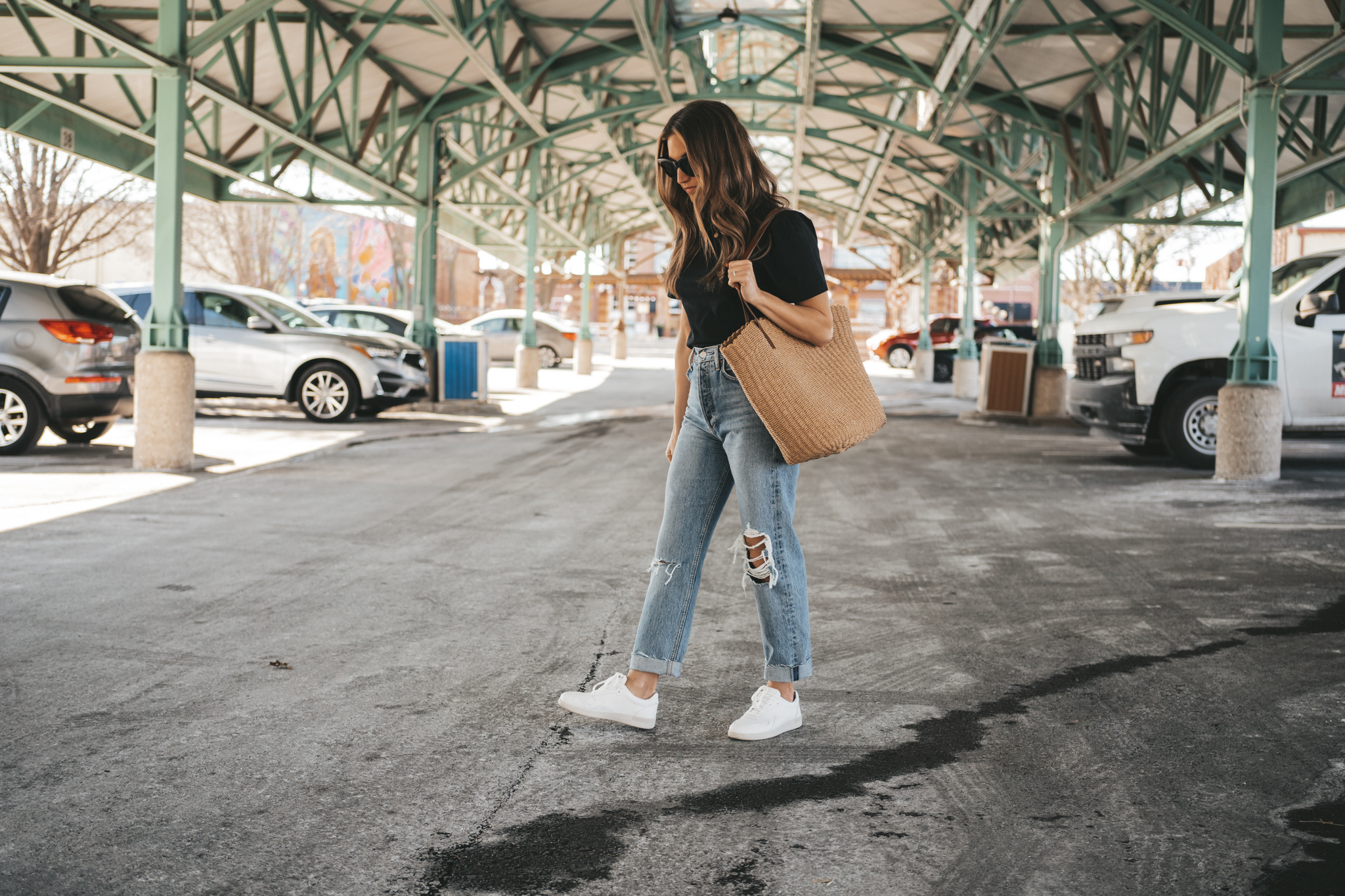 ashley wearing pieces from her spring capsule wardrobe including a black puff sleeve tee, distressed denim, and white sneakers walking through an outdoor pavillion