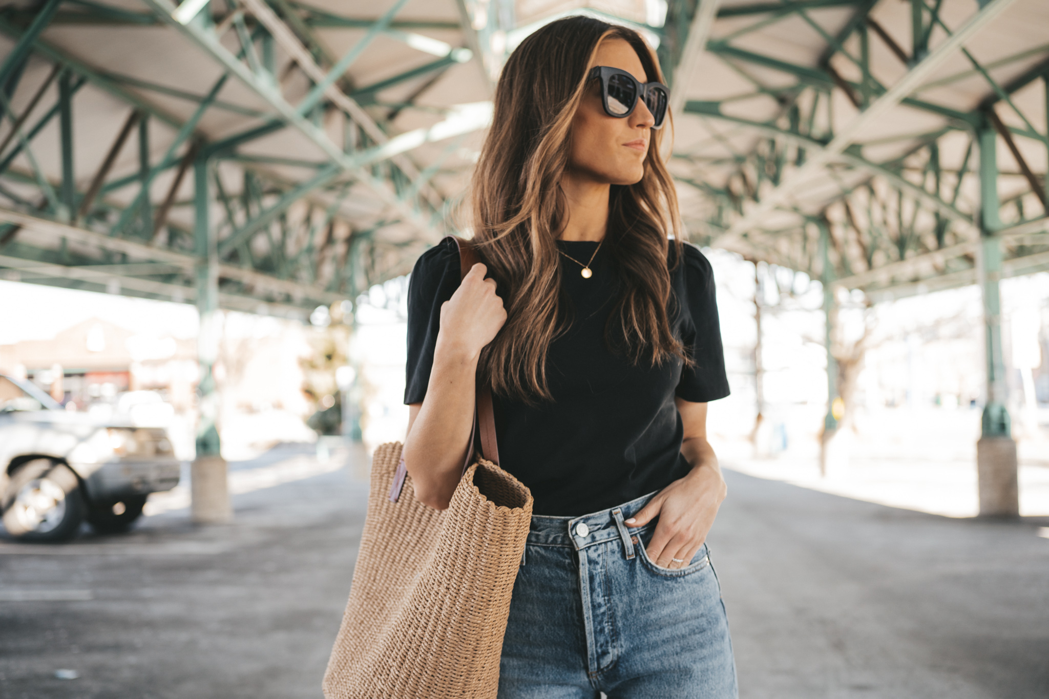 ashley wearing pieces from her spring capsule wardrobe including a black puff sleeve tee, distressed denim, and white sneakers walking through an outdoor pavillion