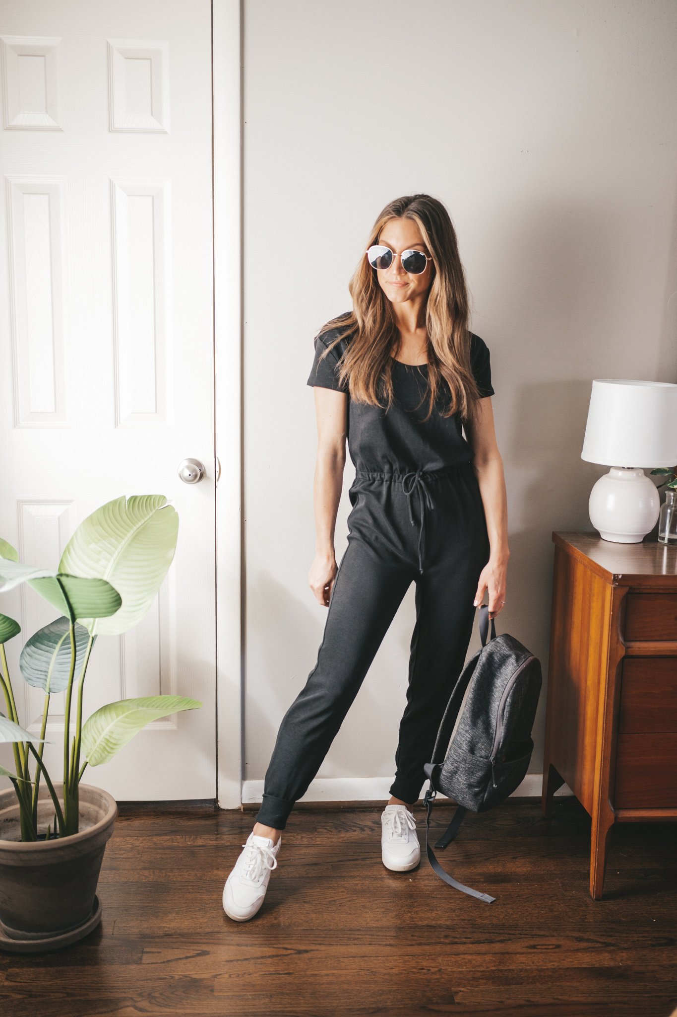 spring break outfit with a black drawstring jumpsuit, sneakers, and a gray backback