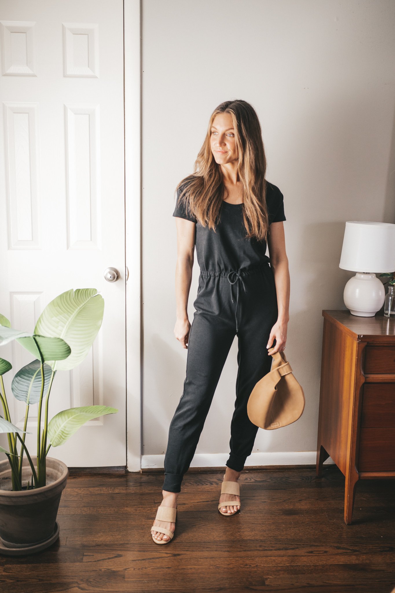 spring break outfit with a black drawstring jumpsuit, woven heeled sandals, and a tan leather clutch