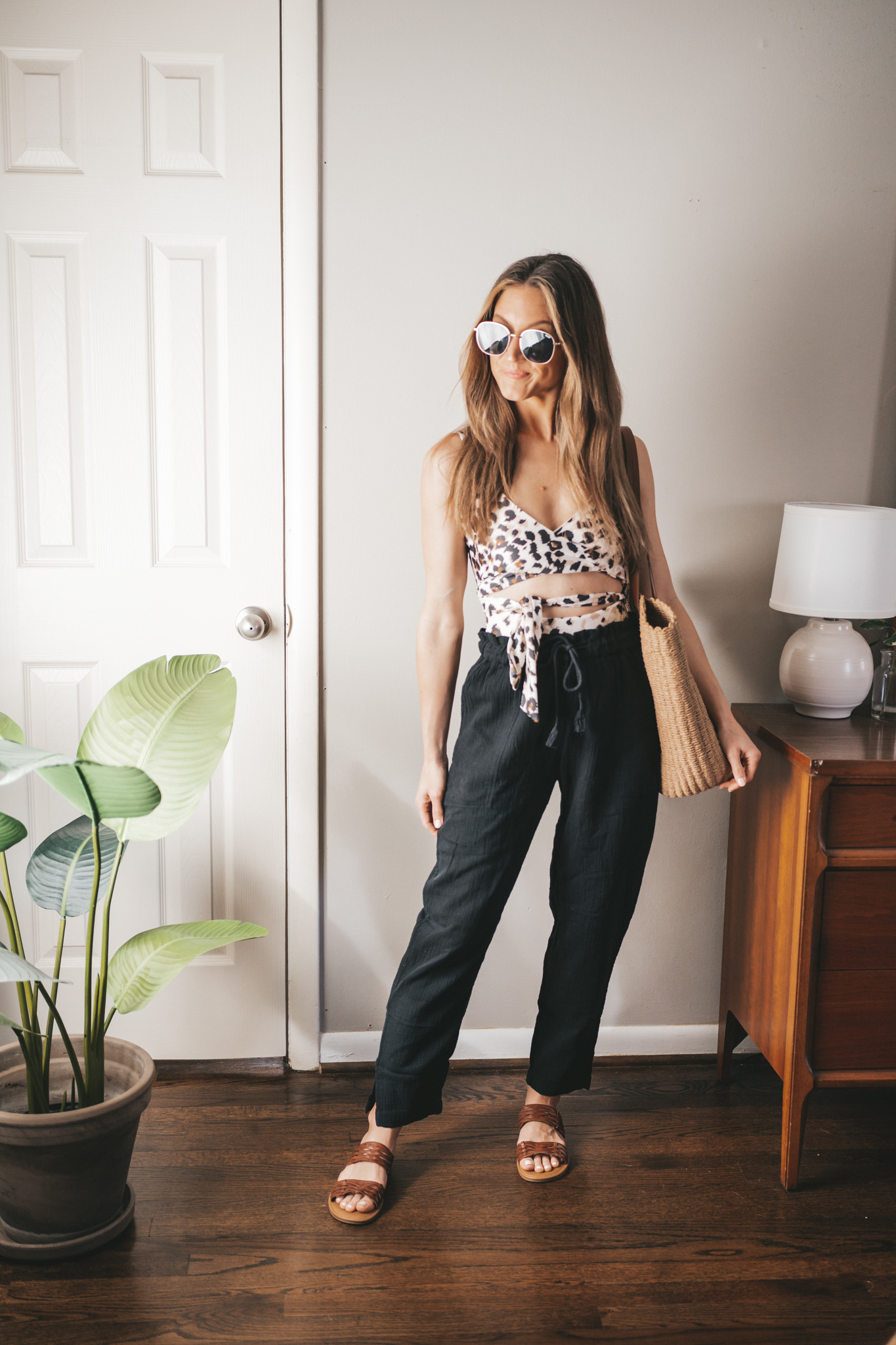 spring break outfit with a leopard print one piece swimsuit, black gauze pants, braided sandals, and a straw tote bag