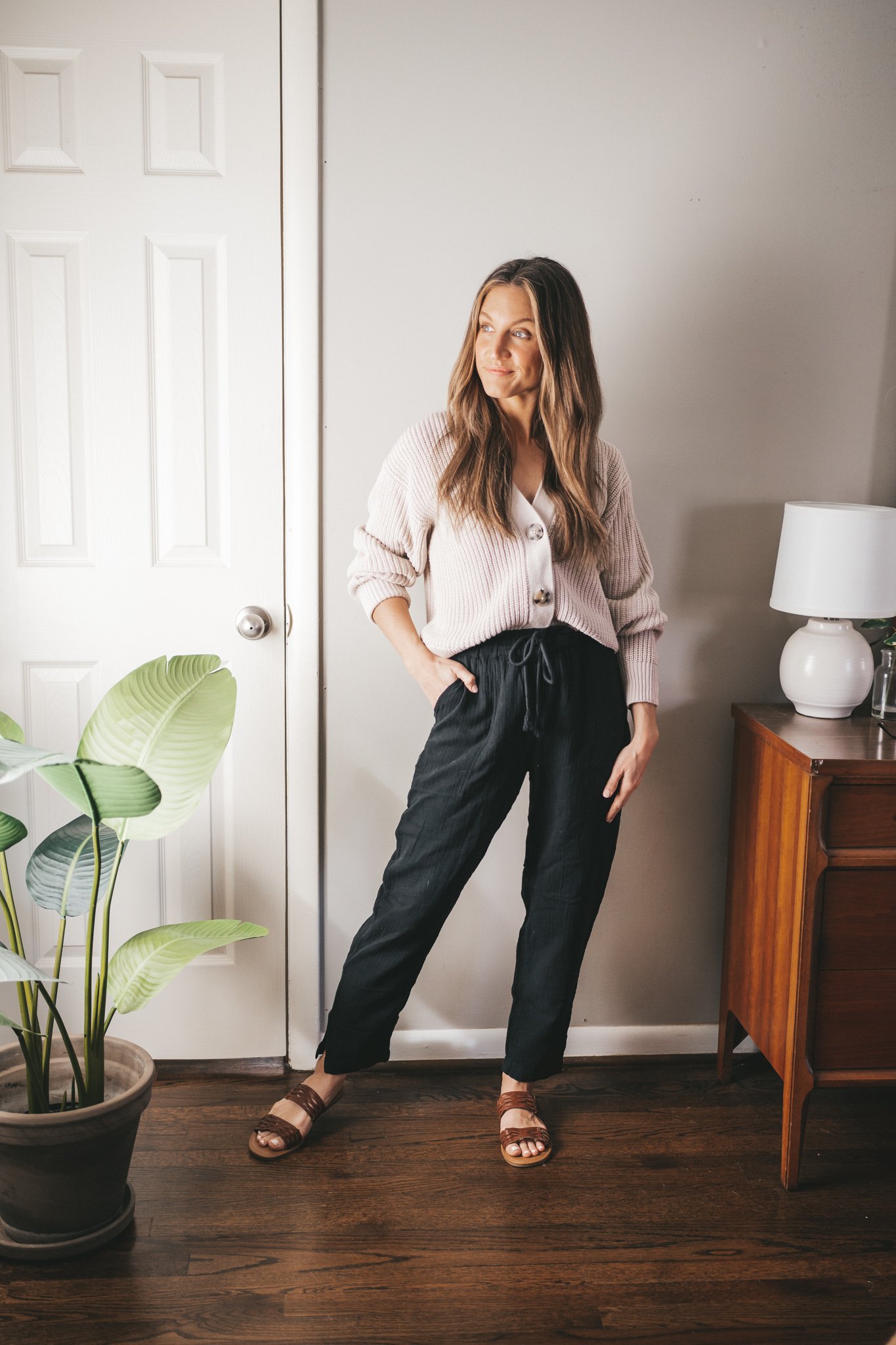 spring break outfit with a taupe cropped button front cardigan, black gauze pants, and braided sandals