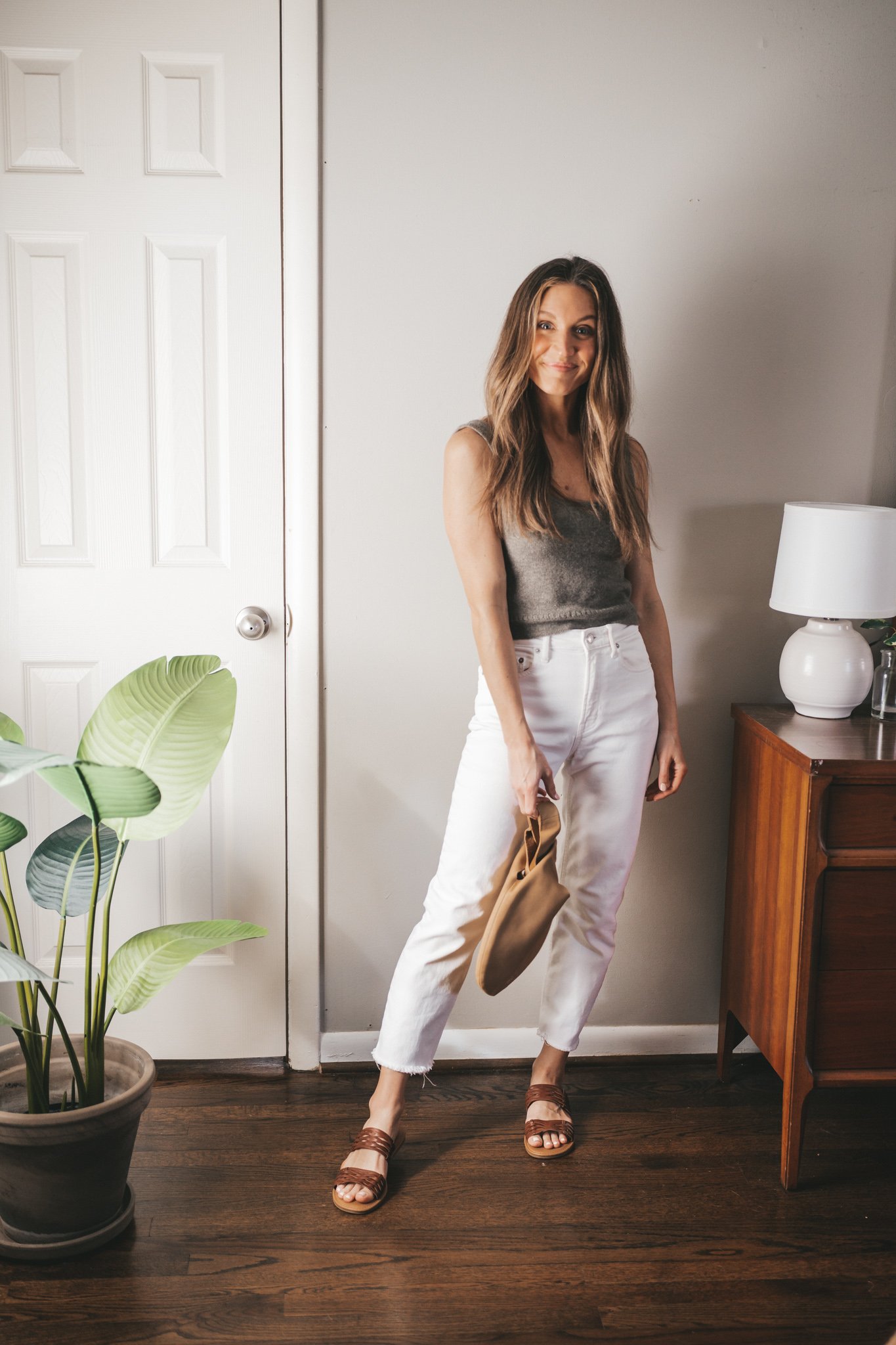 spring break outfit with a taupe sweater tank, white denim, and braided sandals with a tan leather clutch