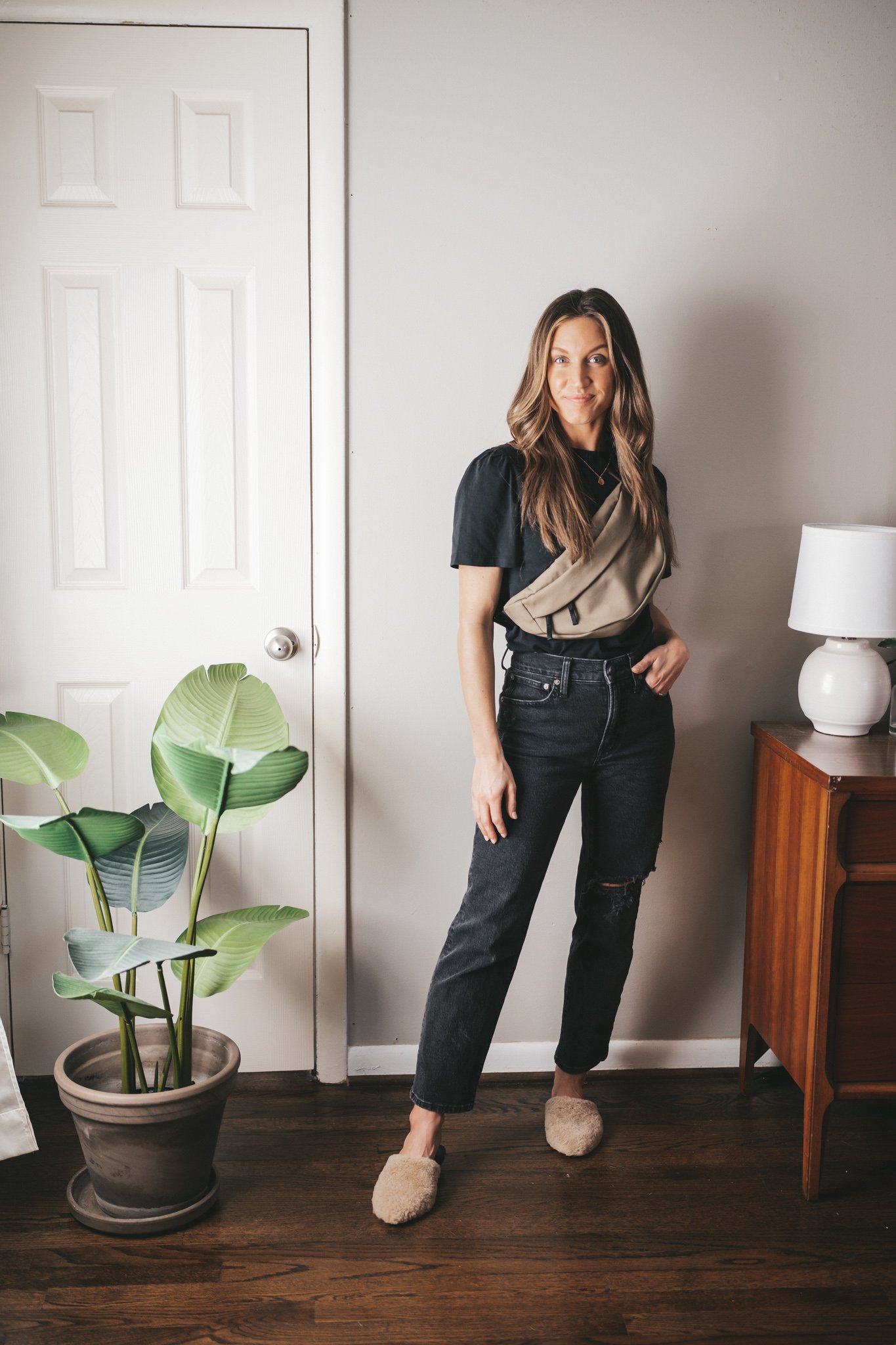 spring capsule wardrobe outfit with a black puff sleeve tee, black distressed denim, tan shearling mules, and an olive green belt bag