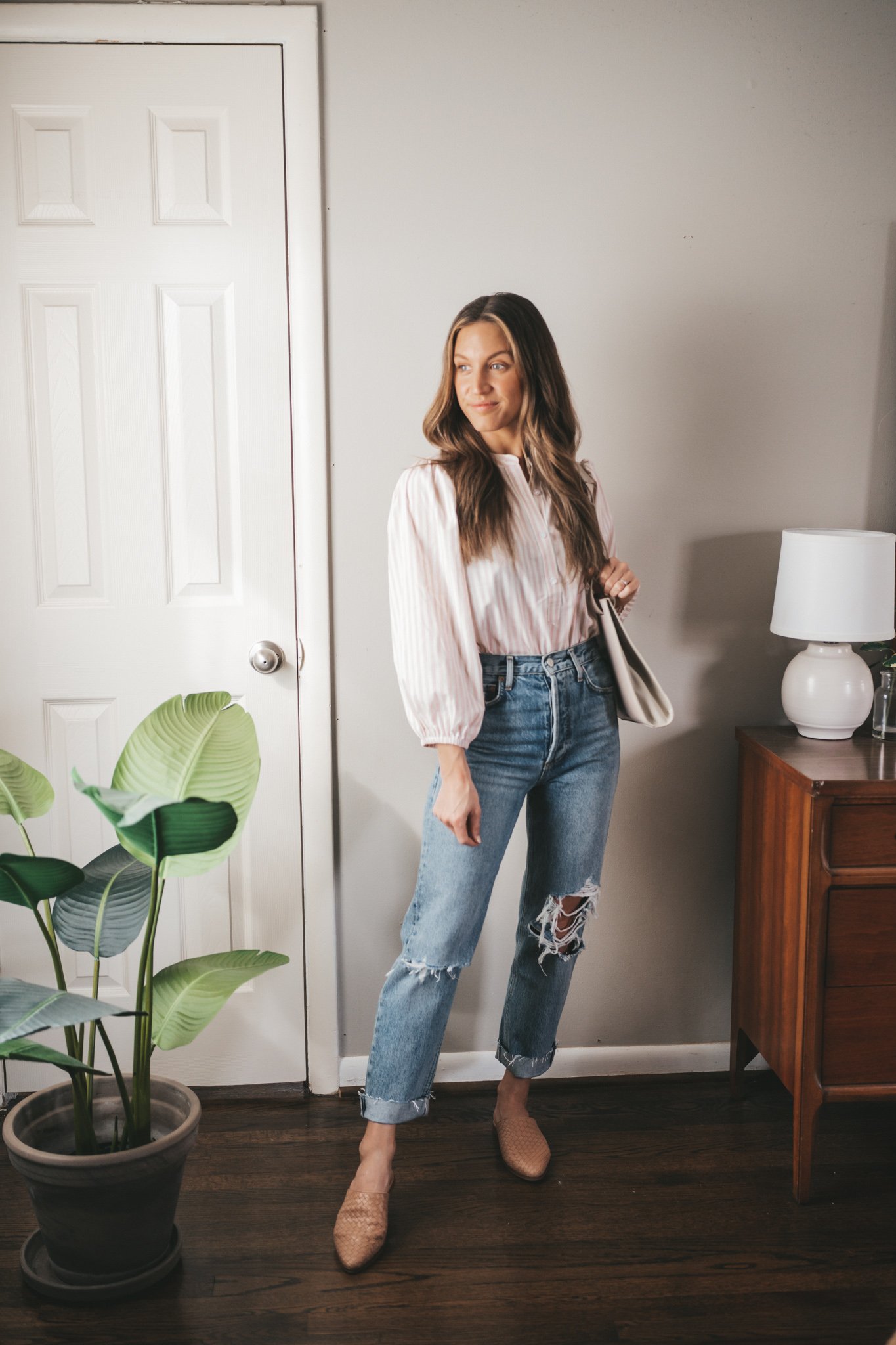spring capsule wardrobe outfit with a tan and white striped blouse, distressed denim, woven mules and a gray shoulder bag