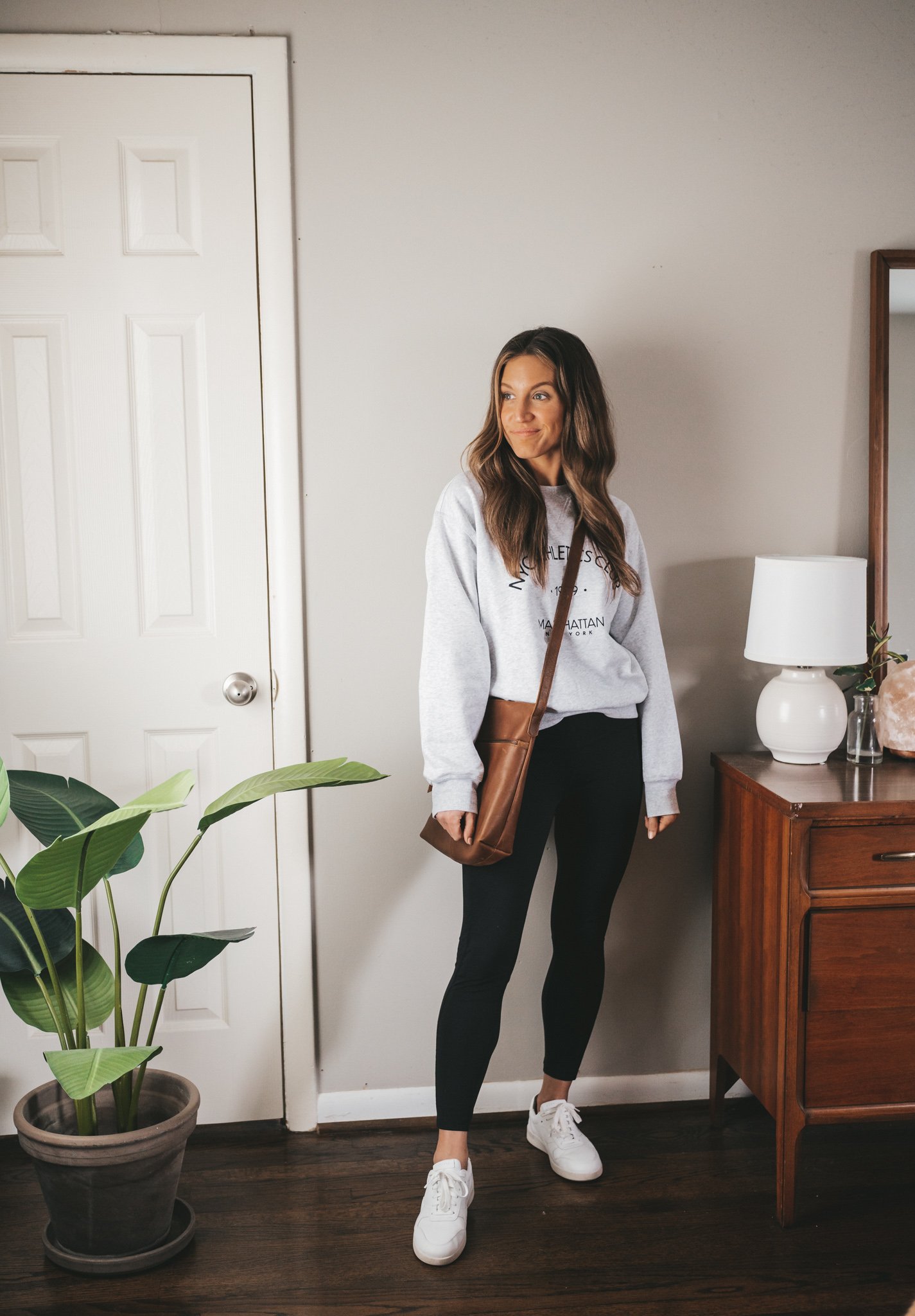 outfit from my spring capsule wardrobe with a gray graphic sweatshirt, black leggings, and white sneakers with a brown crossbody bag