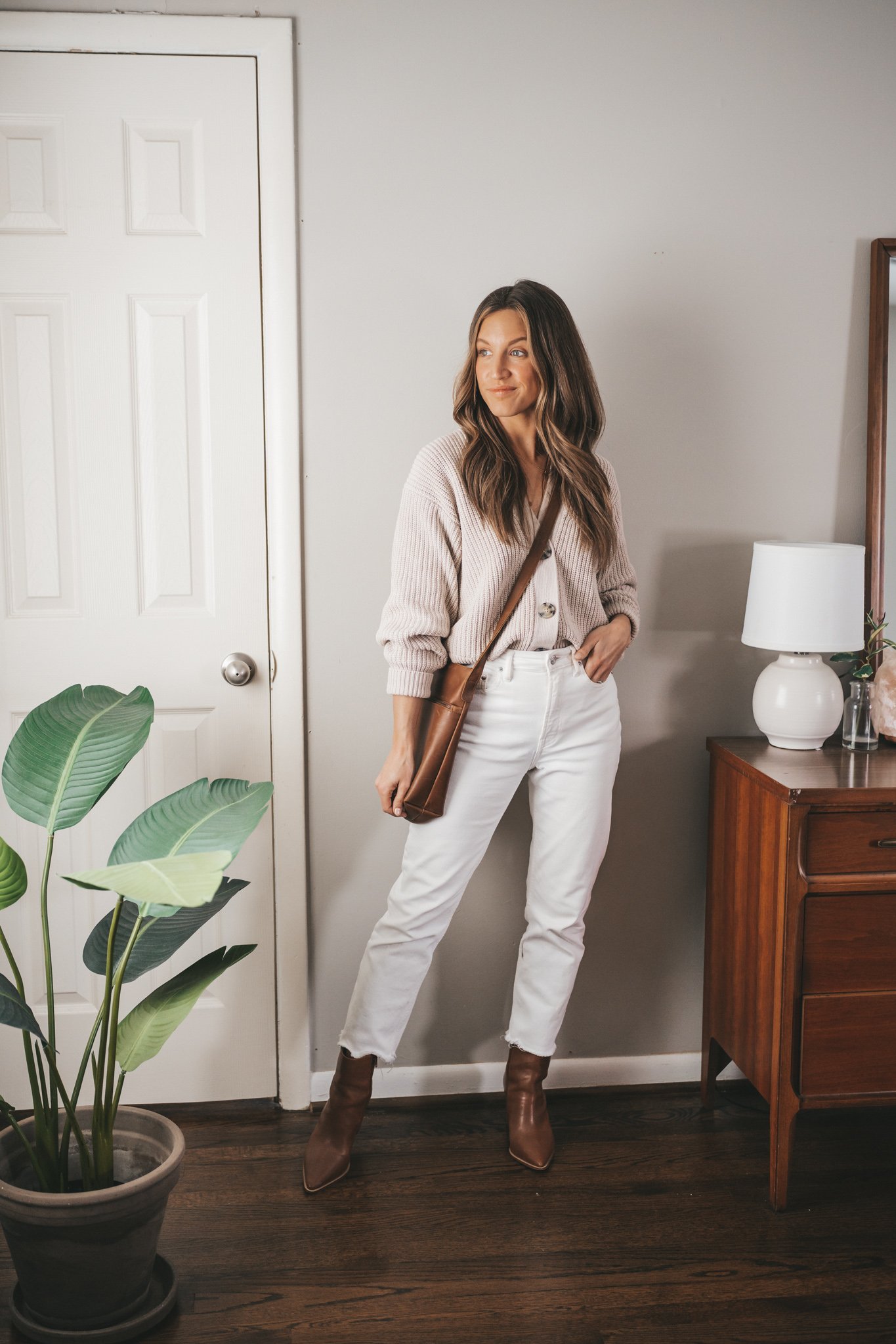 spring capsule wardrobe outfit with a taupe button front cropped cardigan, white denim, brown heeled ankle boots, and a brown crossbody bag