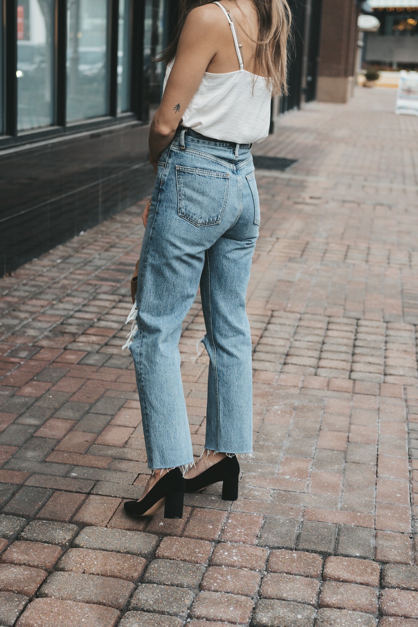 ashley wearing the agolde 90s pinch waist denim which a silk cami, black blazer, and black block heel pumps with a tan leather clutch bag walking down a paved sidewalk in front of some shops