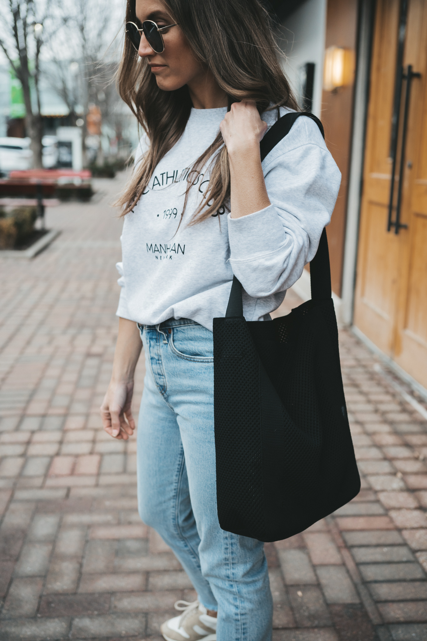 ashley wearing a gray graphic sweatshirt, light wash mom jeans, tan leather sneakers, oversized gold frame sunglasses and a black tote bag